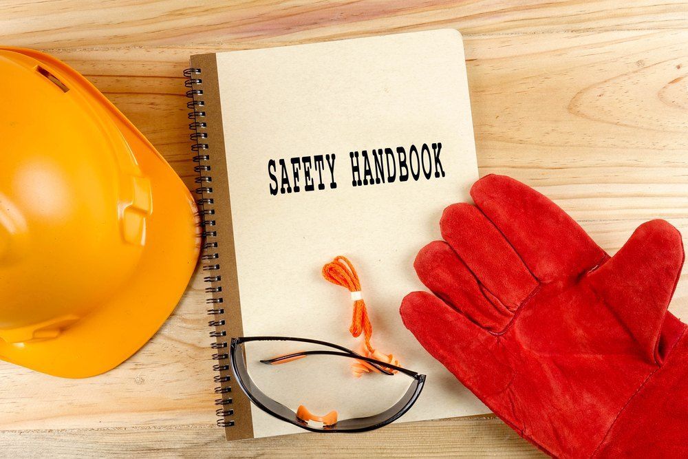 A Safety Handbook is on a Wooden Table Next to a Hard Hat and Gloves — Signtek Gladstone in Gladstone Central, QLD