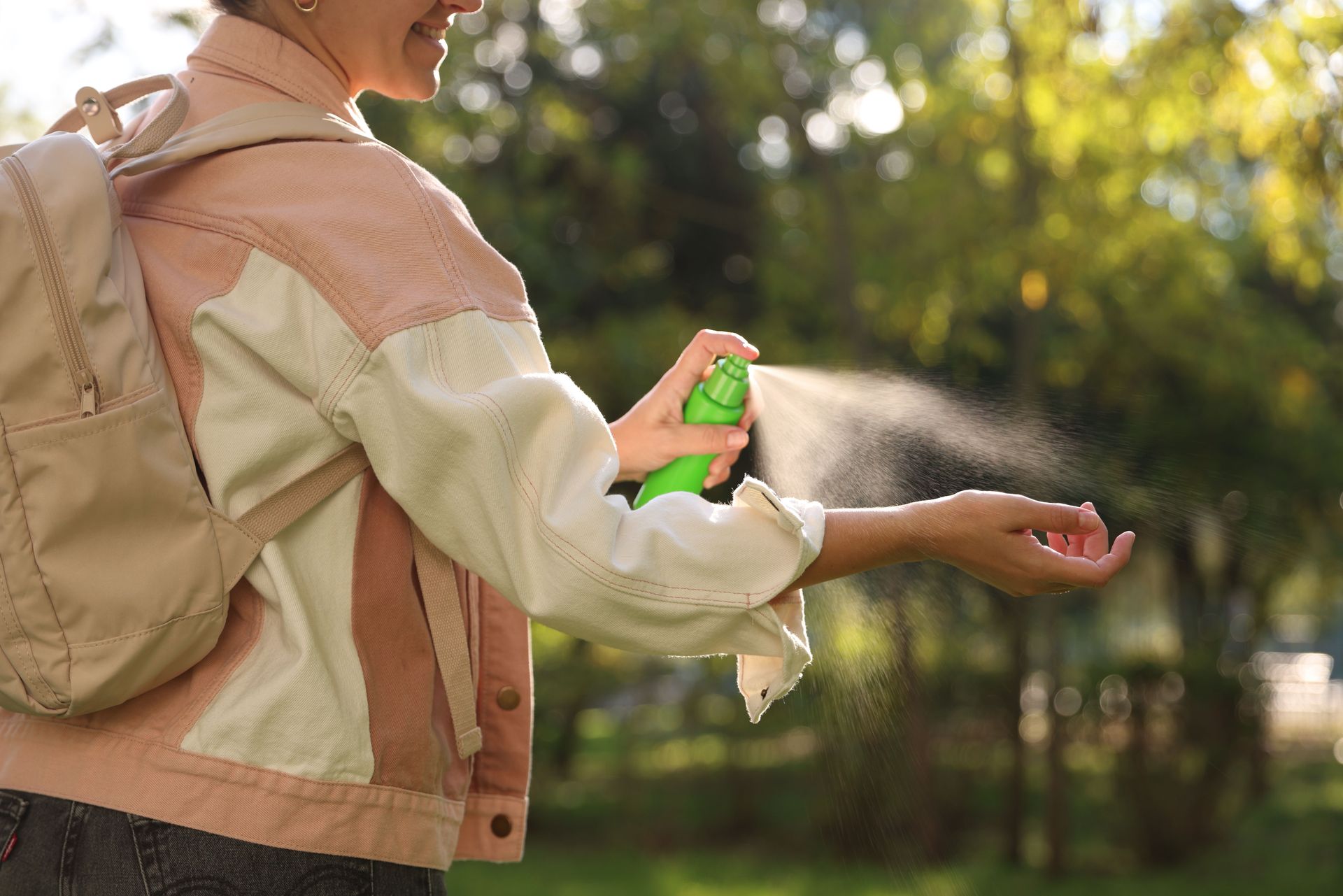 Person spraying sanitizer on outstretched hands outdoors in sunlight