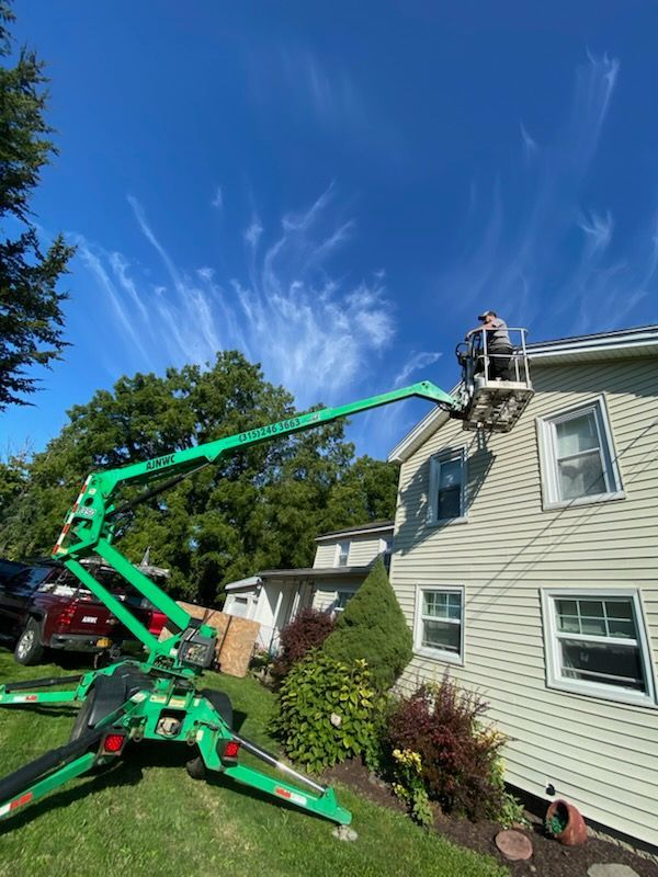 Green lift extending to a two-story house, person in the lift, working on the roof. Bright blue sky.