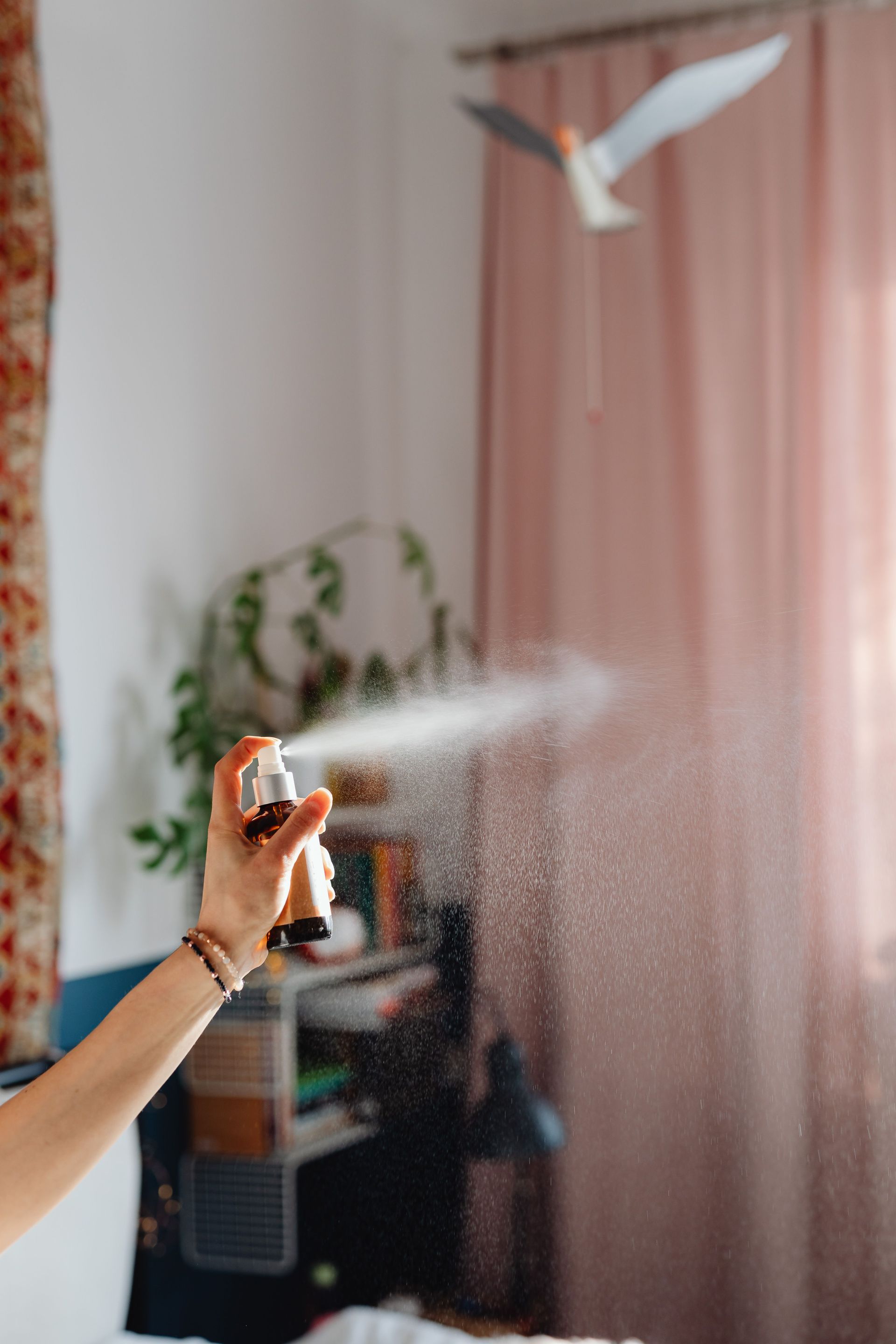 Hand spraying mist toward a white dove in a pink-curtained room
