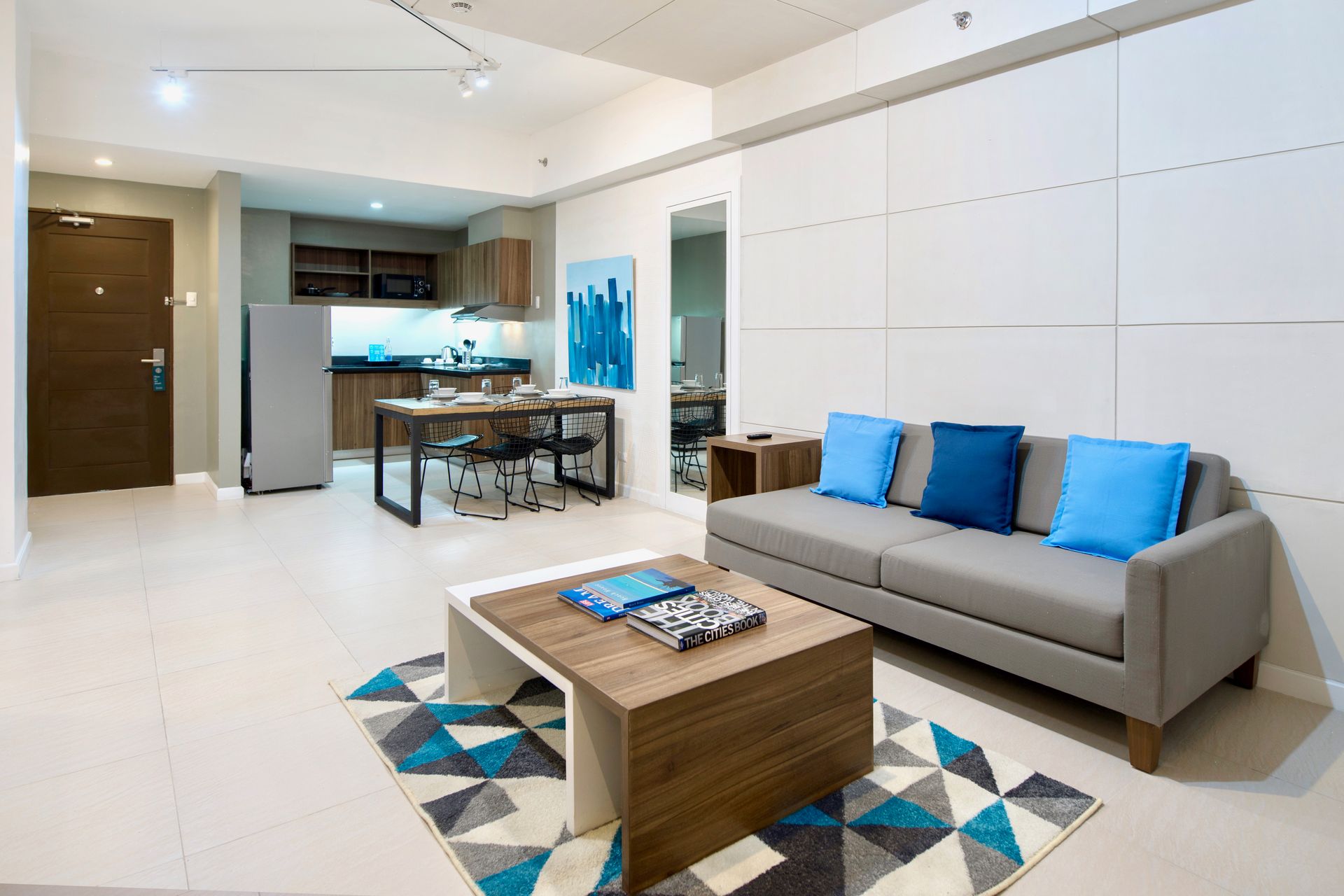 Modern living room with gray sofa, blue pillows, wooden coffee table, and open kitchen in the background