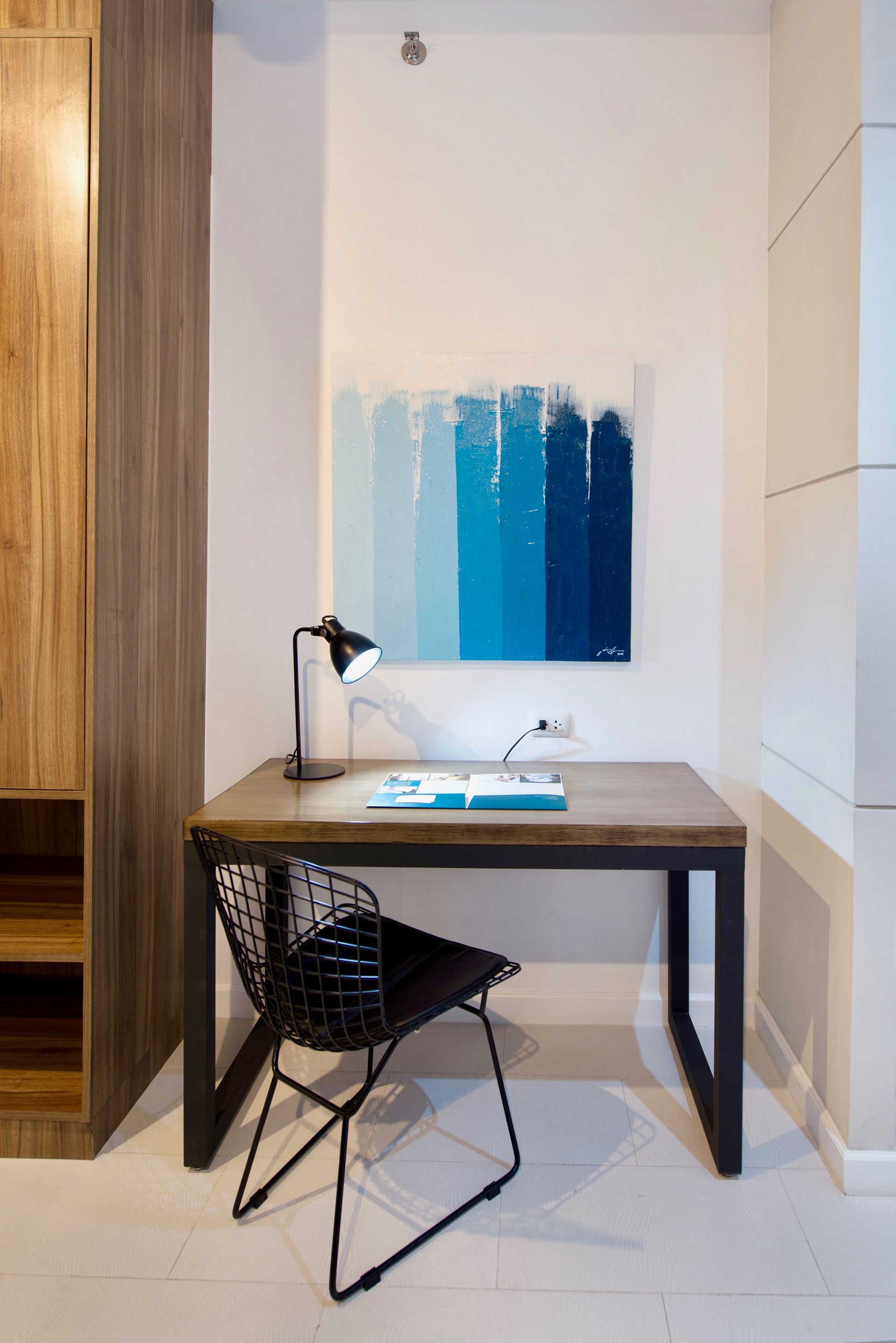 Work desk with a black lamp and wire chair in a serviced apartment at The Sphere Makati, below blue abstract art