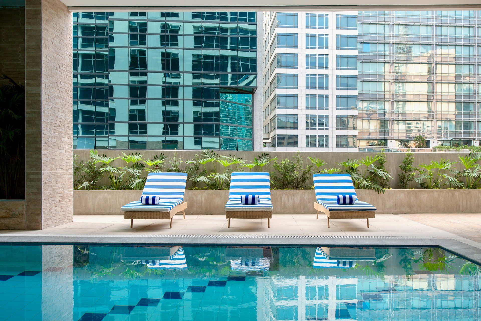 Modern pool with blue lounge chairs and city buildings reflected in the water
