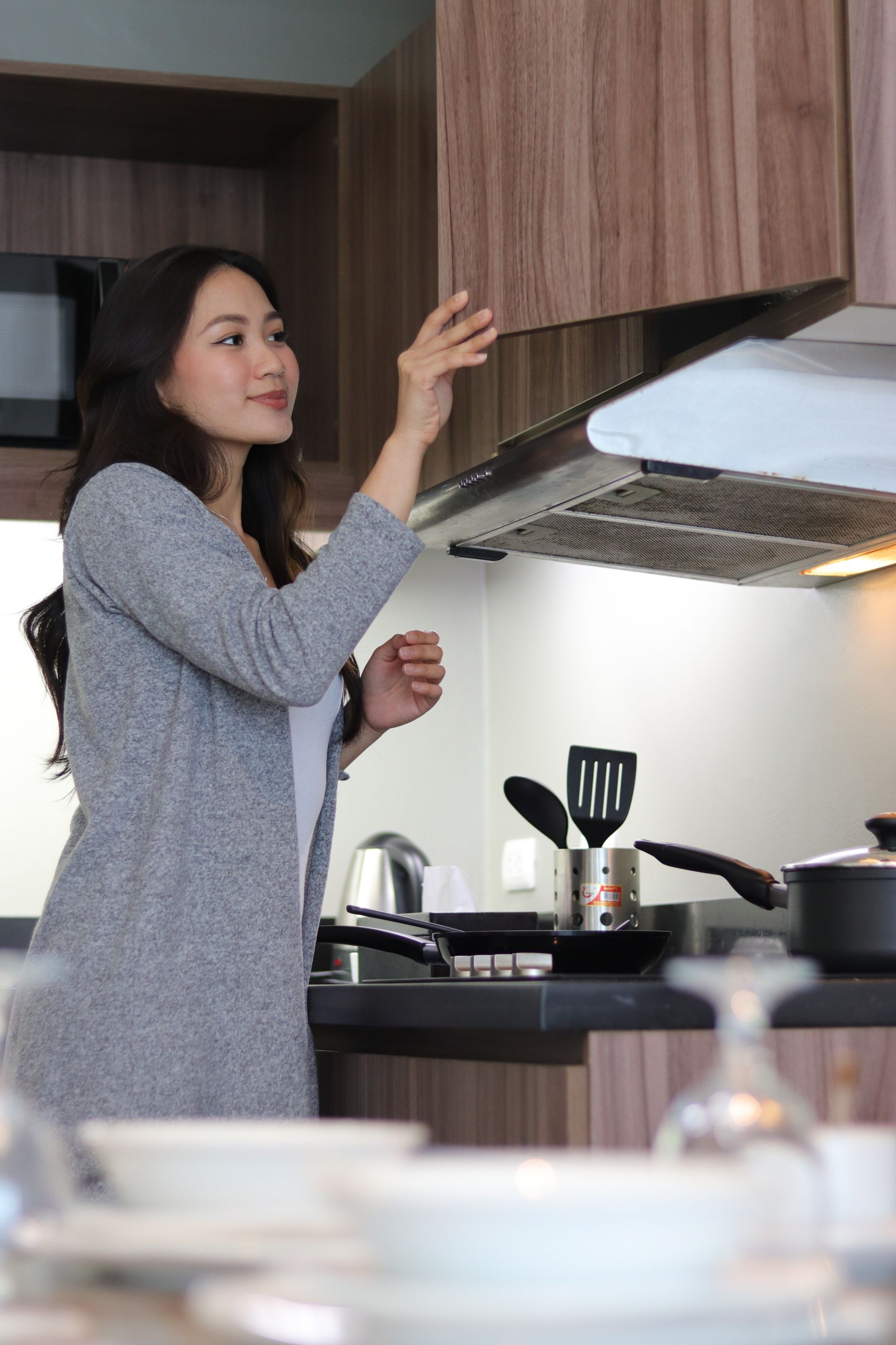 Woman reaching for a cabinet in a modern spacious kitchen while cooking at the stove