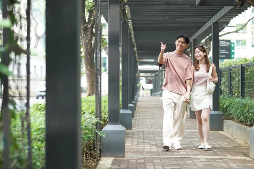 Couple strolling under a covered walkway, man pointing, woman holding a bag, smiling.