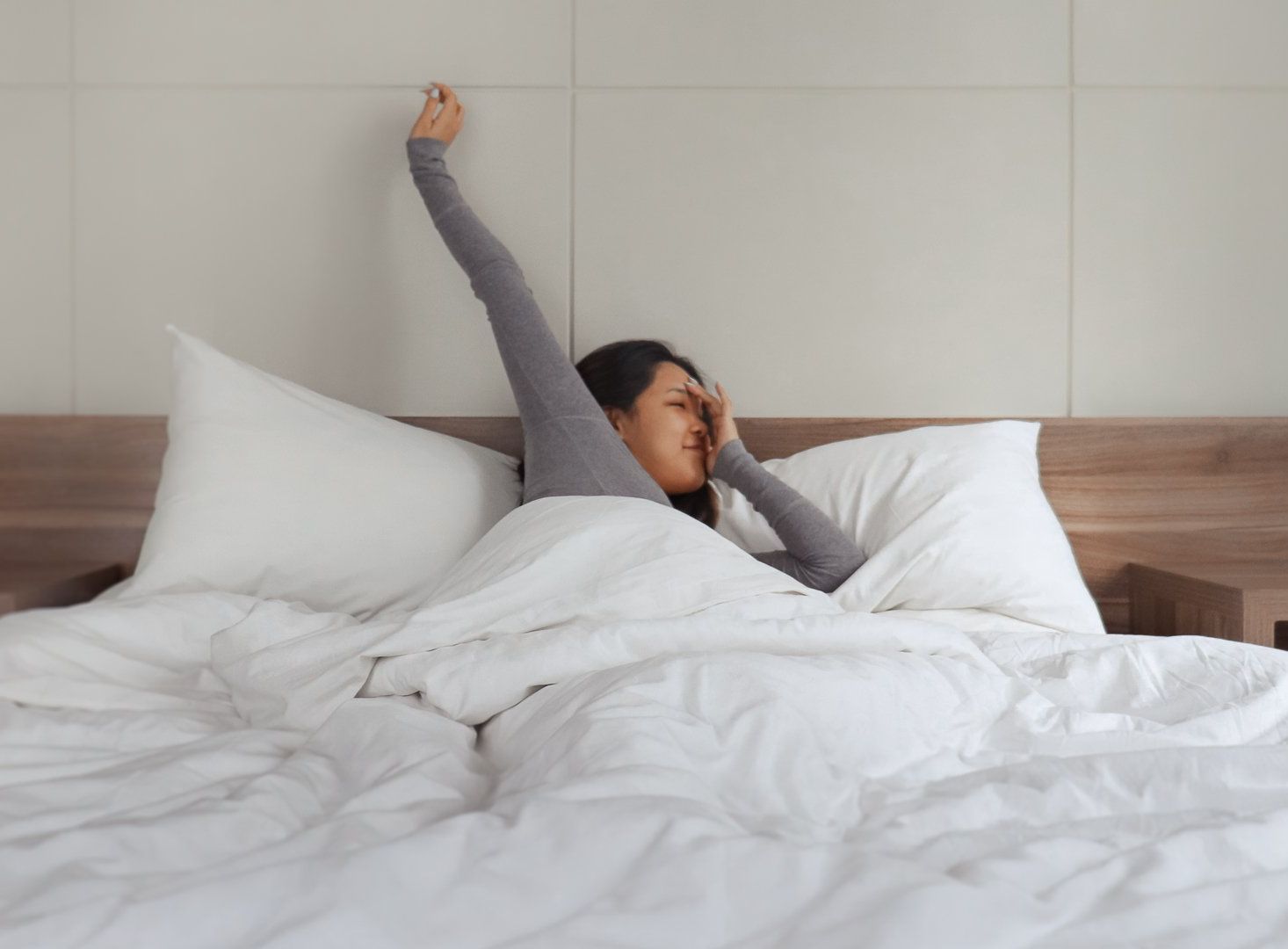 A woman is sitting on a bed stretching her arms.