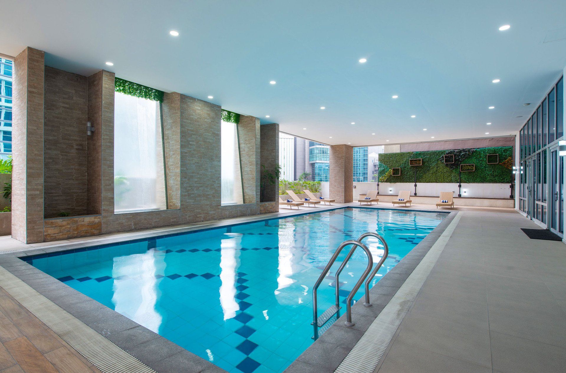 Indoor swimming pool with clear blue water, stone wall feature, and lounge chairs.