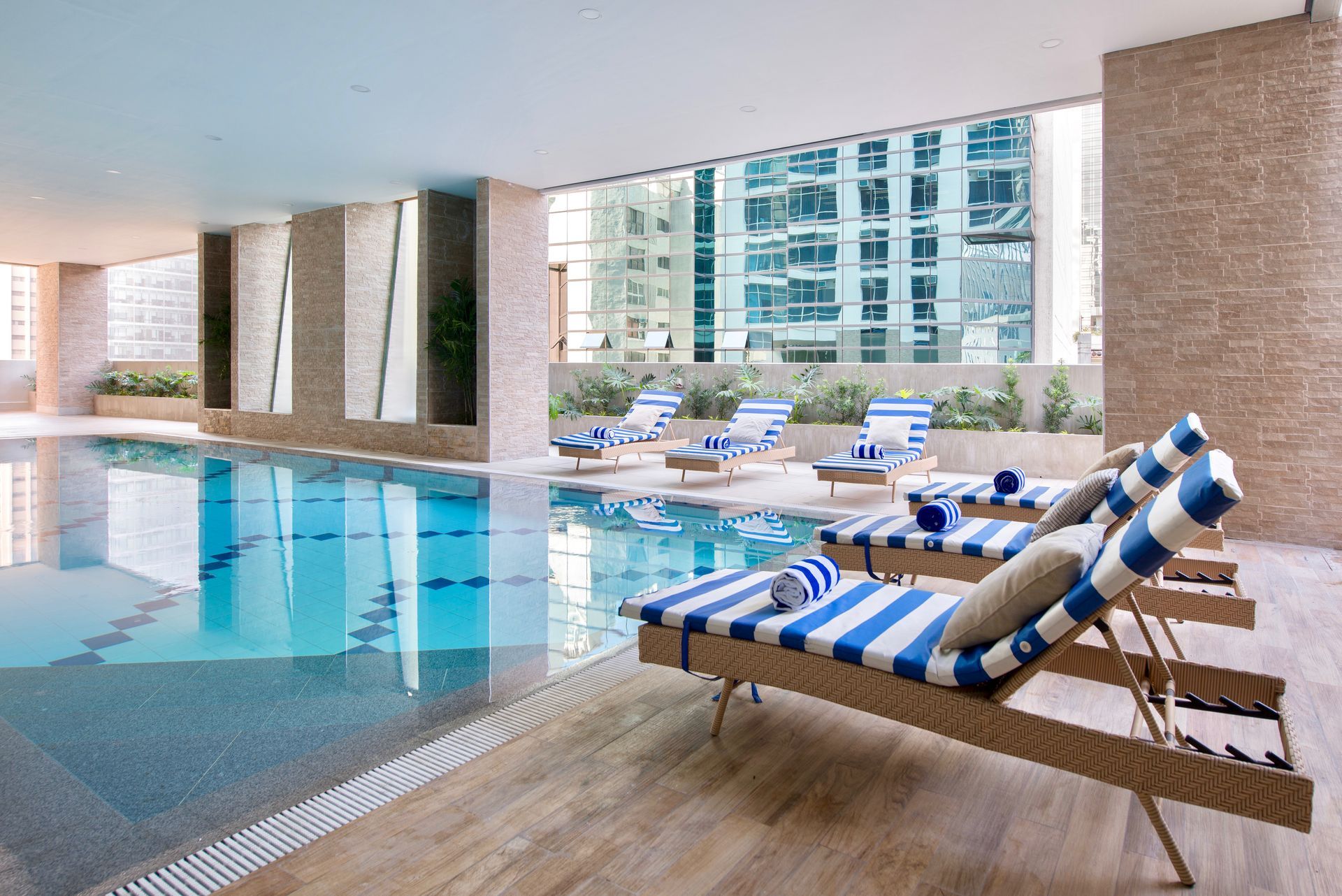 Covered hotel pool area on the rooftop with blue-striped lounge chairs and city-view windows