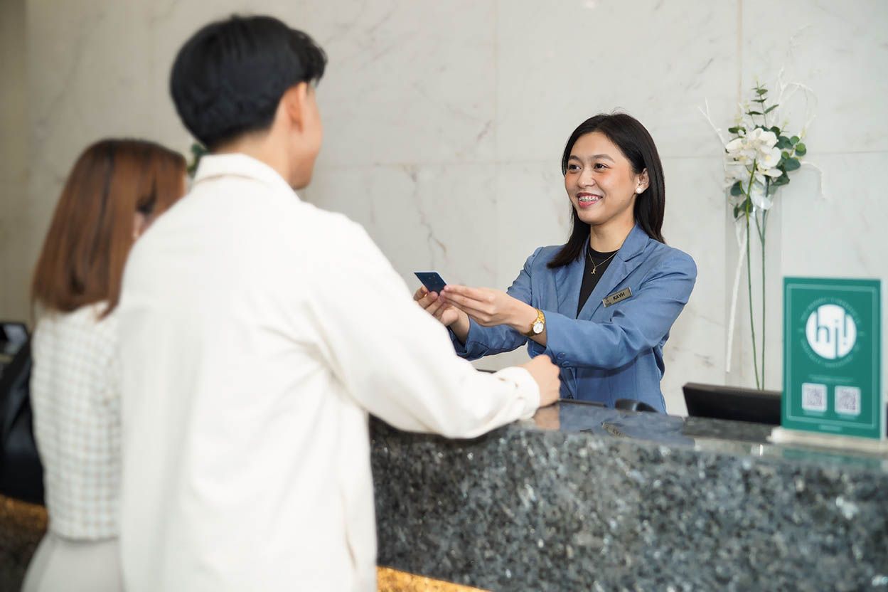 Couple checking in at a hotel reception desk. A smiling receptionist hands a keycard over the counter.