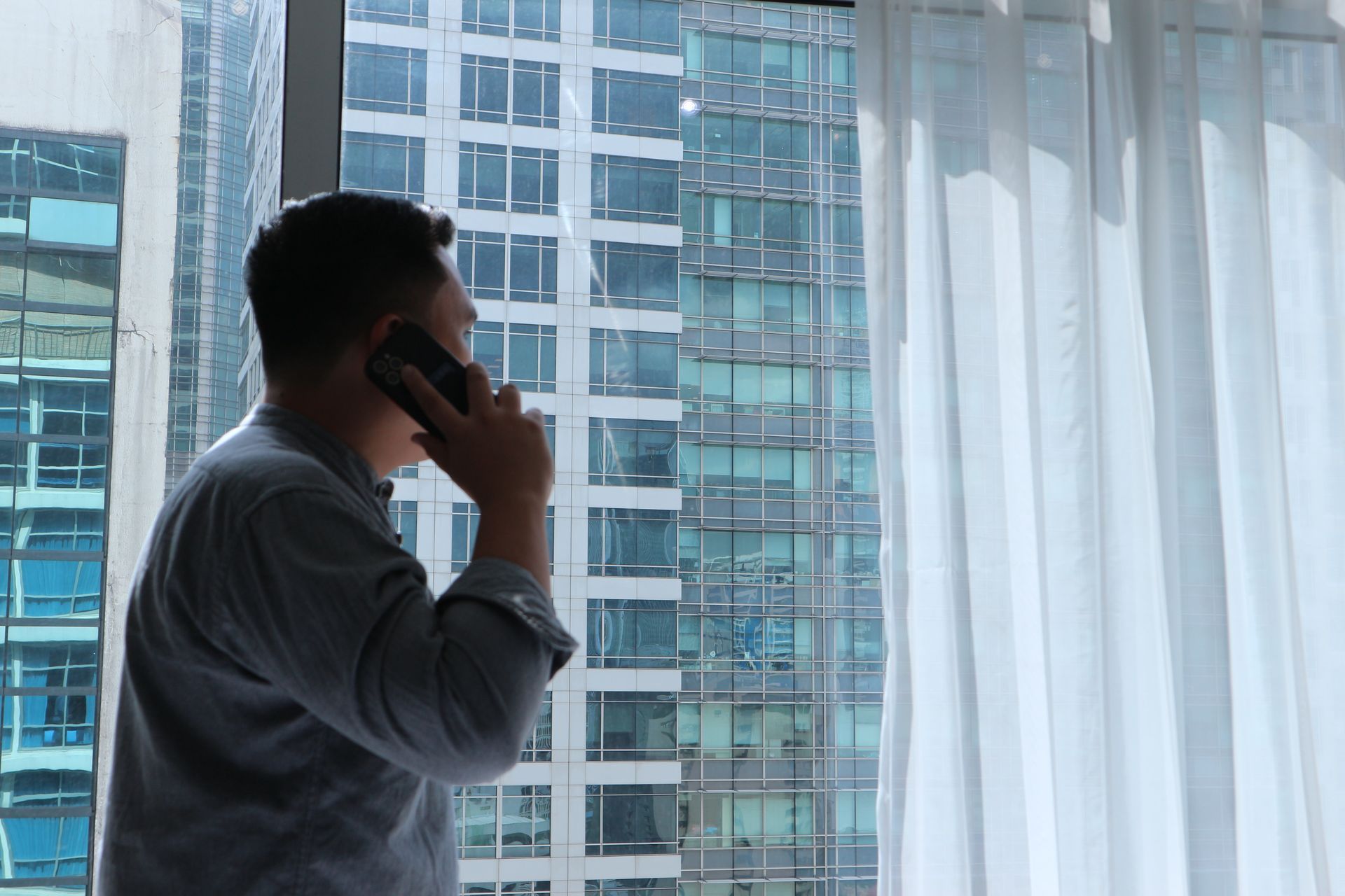 Guest on a phone call by the window of a serviced apartment at The Sphere Makati overlooking city high-rises
