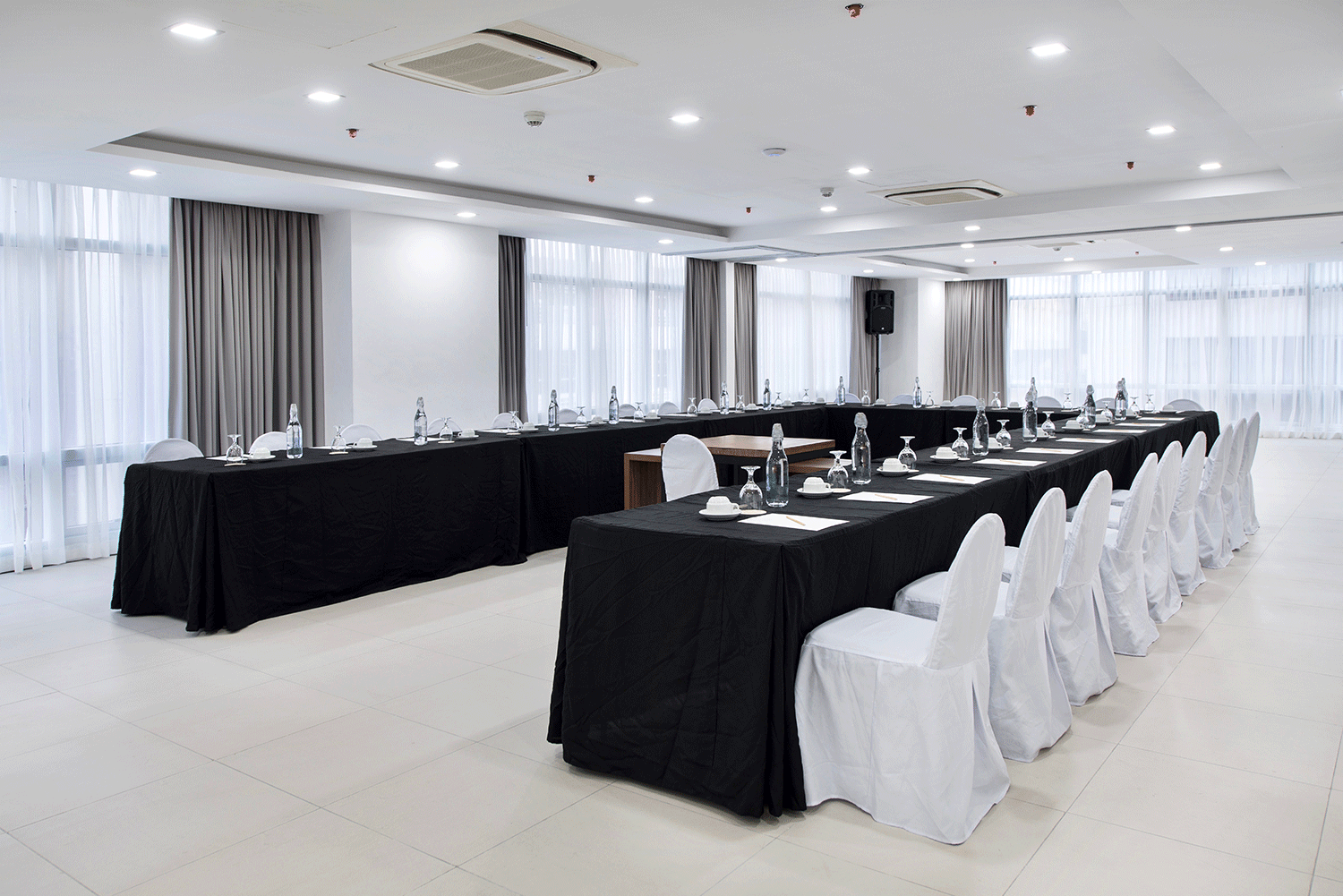 Conference room with a U-shaped table, black tablecloths, white chairs, and large windows with curtains.