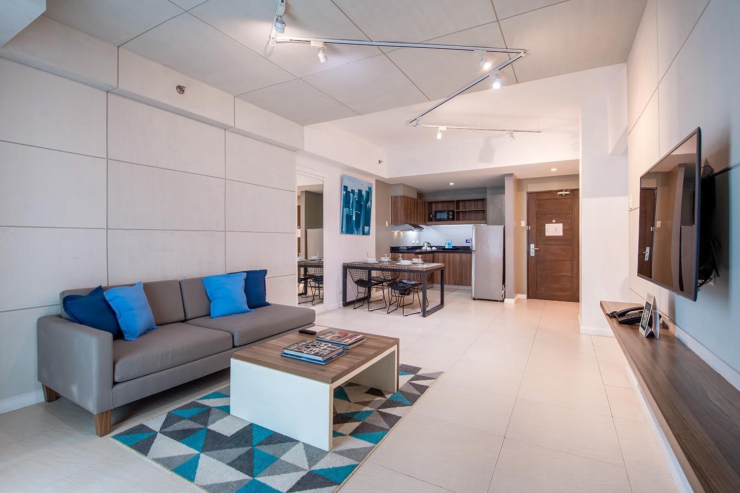 Modern open-plan living room with gray sofa, blue accents, coffee table, and kitchen in the background