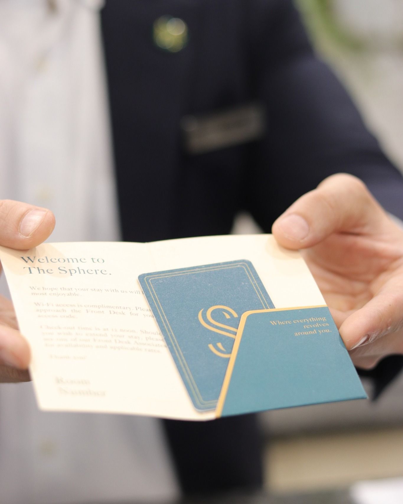 Hands holding a The Sphere booking card and an open booklet over a dark suit jacket