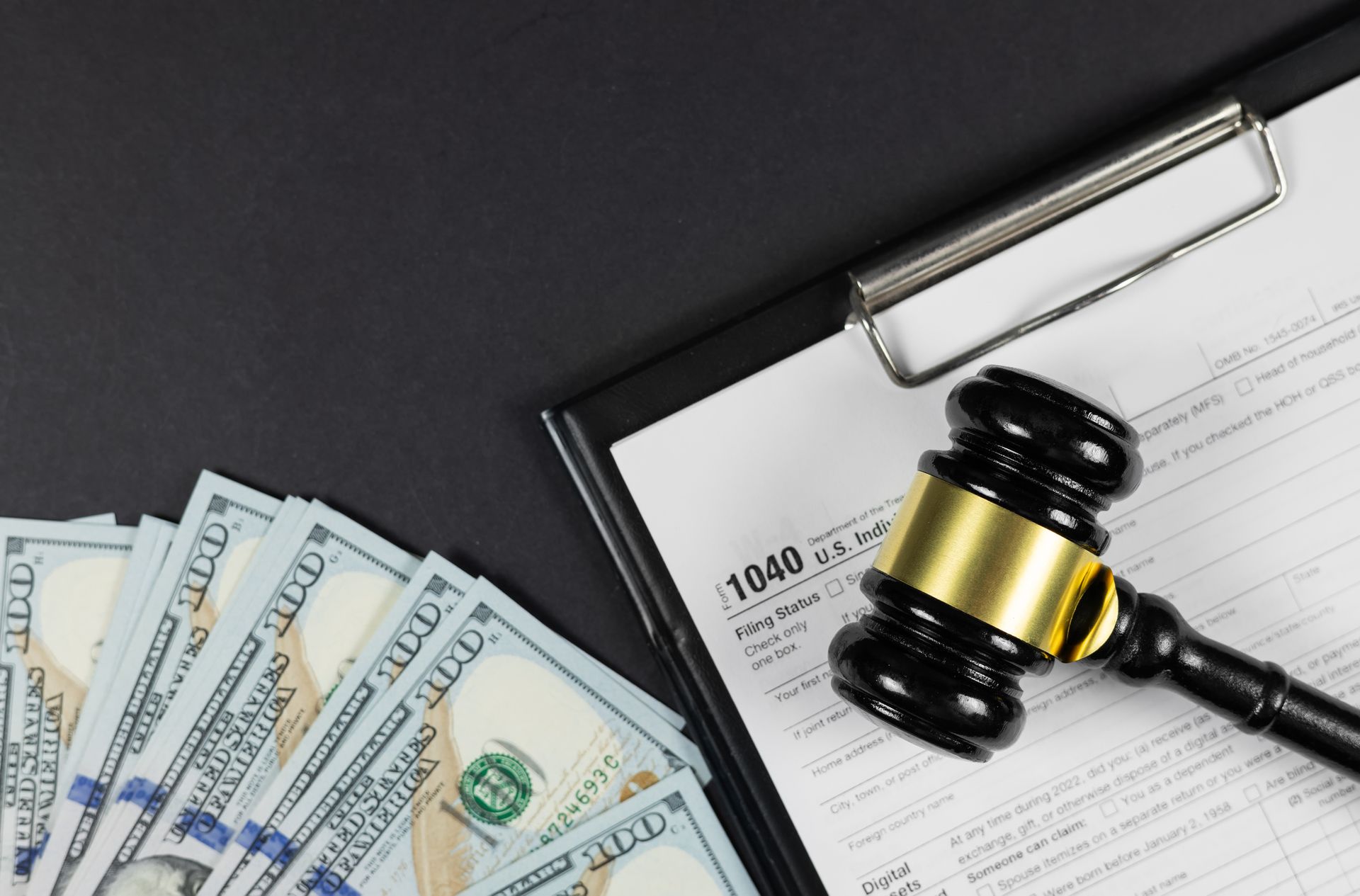 Black gavel on top of tax form with a fan of US dollar bills. Black gavel on top of tax form with a fan of US dollar bills.