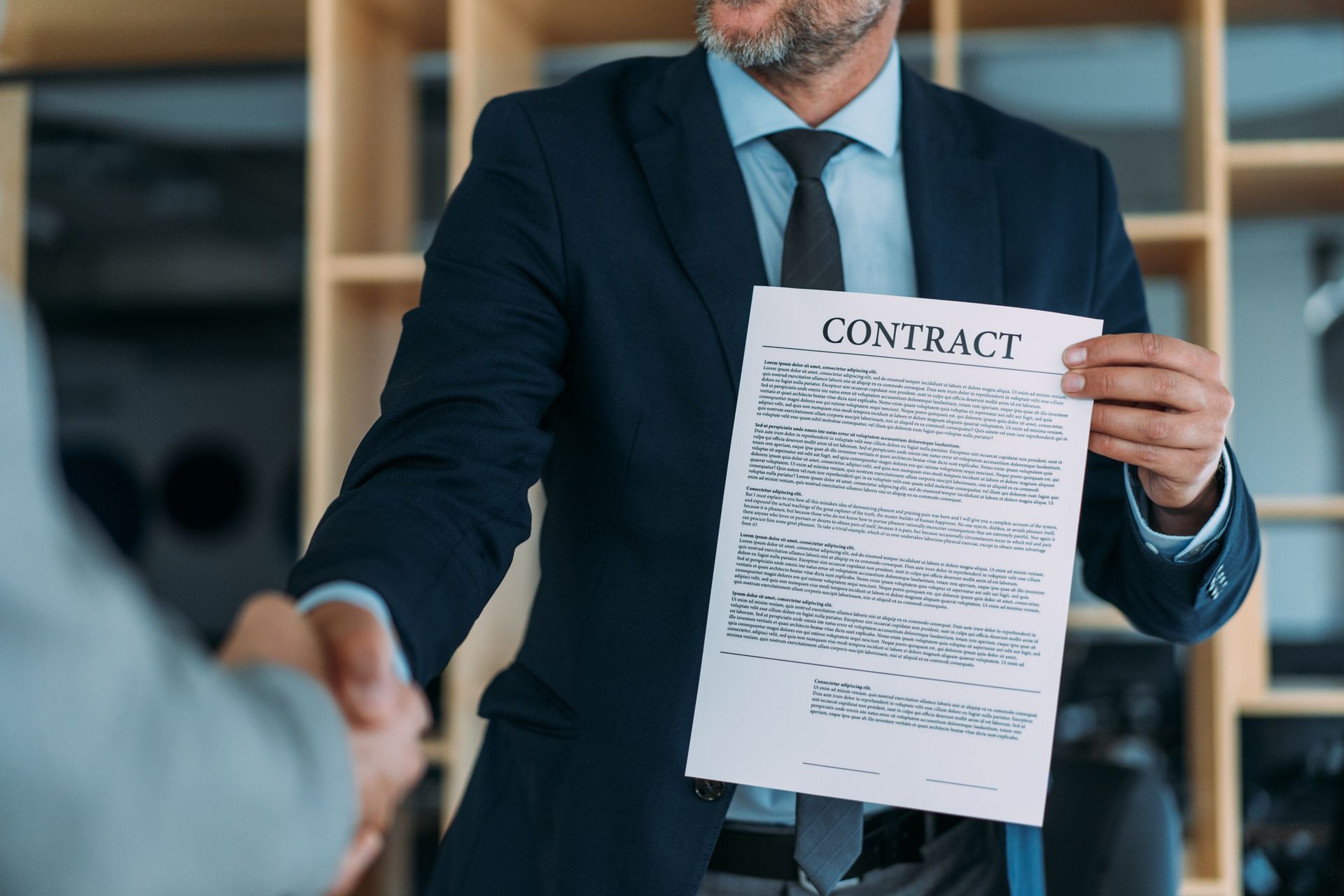 Man in suit holding a contract, shaking hands with another person. Man in suit holding a contract, shaking hands with another person.