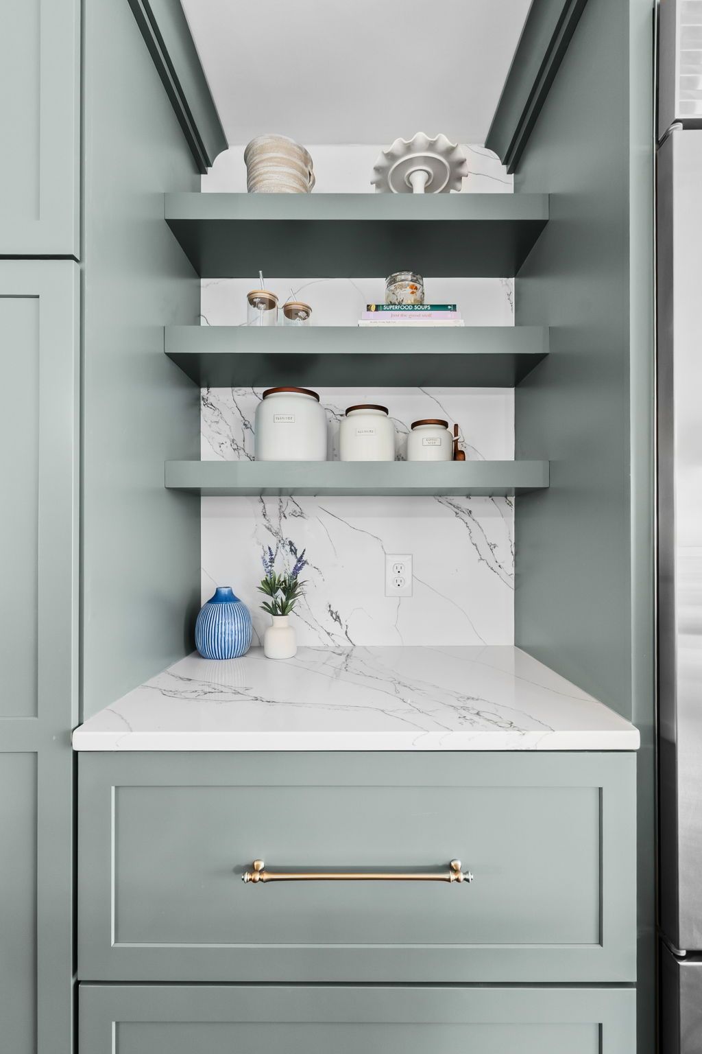 Built-in sage green pantry shelves with white marble countertop and gold drawer pull