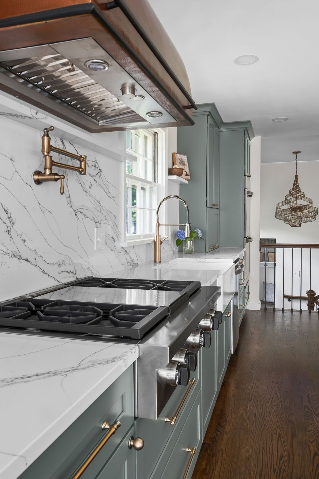 Modern kitchen with teal cabinets, marble backsplash, gas range, white countertops, and dark wood floors