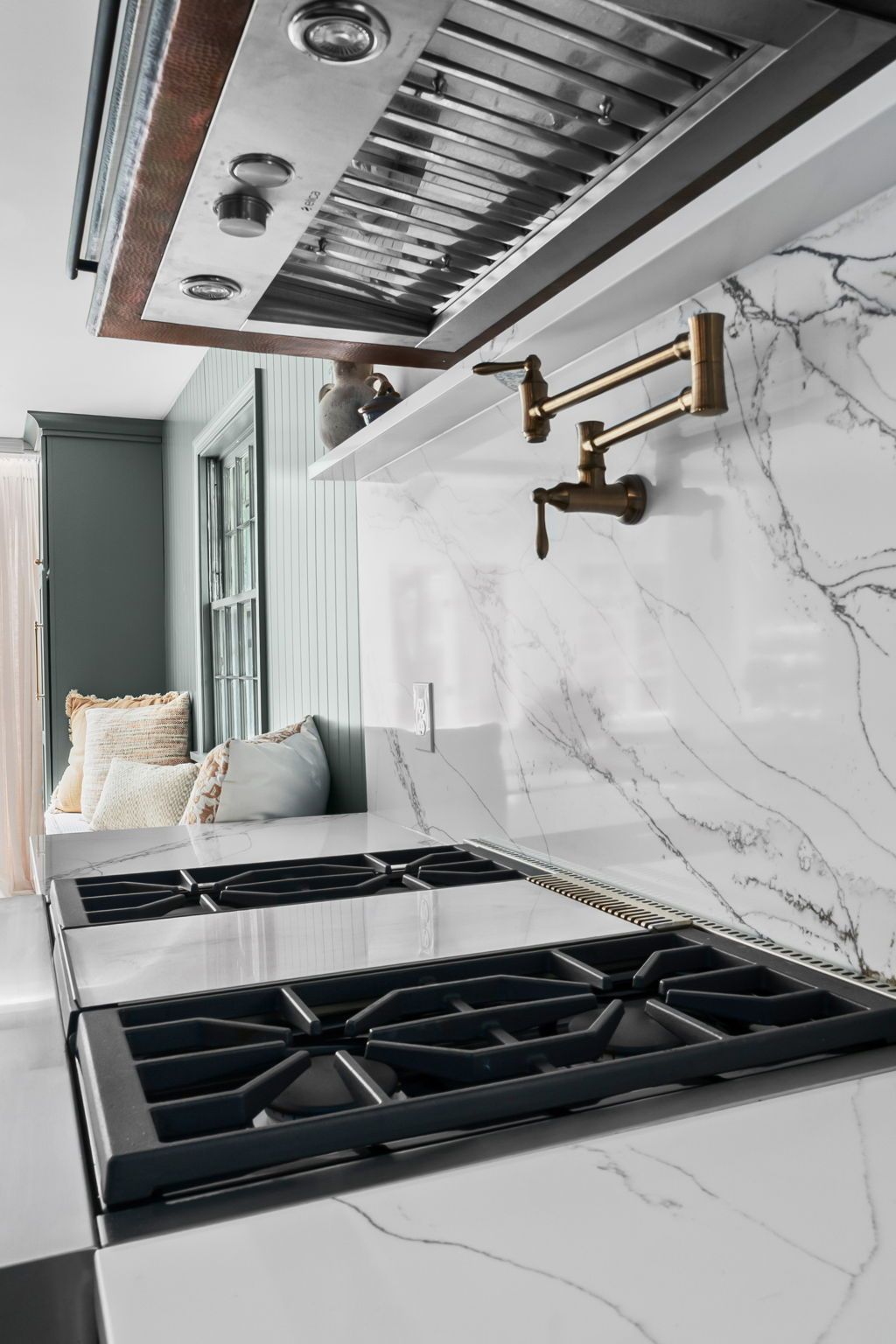 Modern kitchen with white marble backsplash, brass faucet, and black gas cooktop under stainless range hood