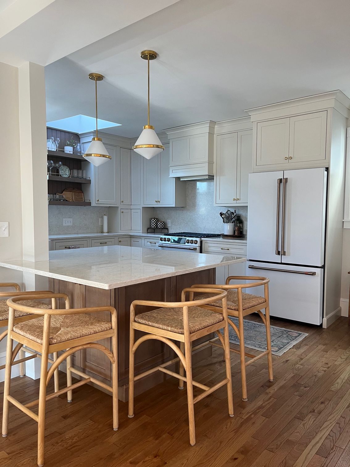 A kitchen with a large island , stools , a refrigerator and a stove.
