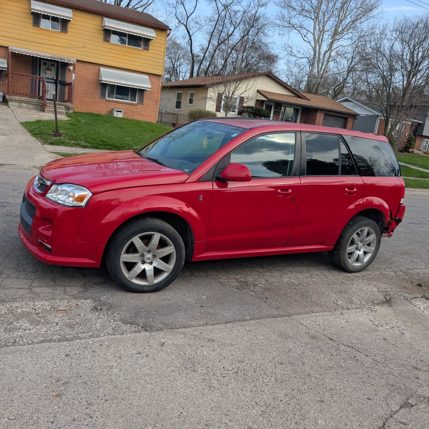 Red SUV parked on a residential street in front of houses and leafless trees.