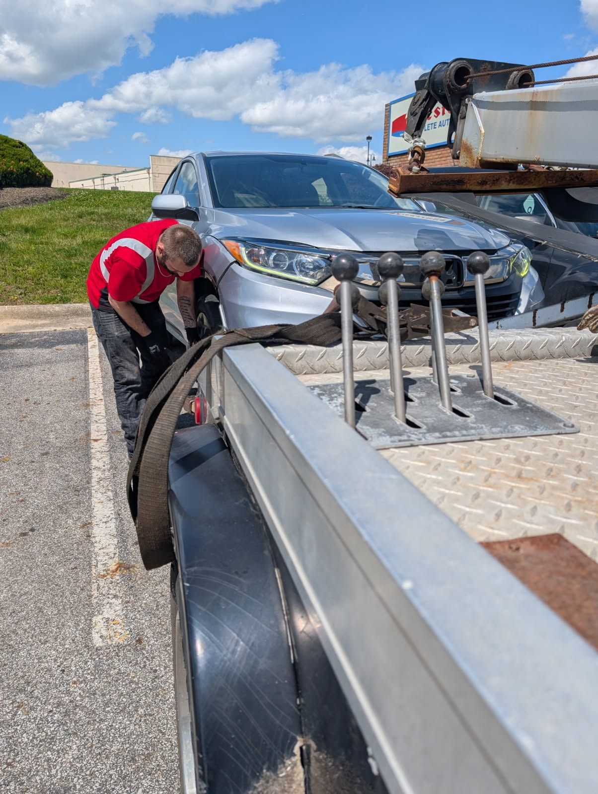 Worker in red shirt adjusting a car on a flatbed tow truck by the roadside.