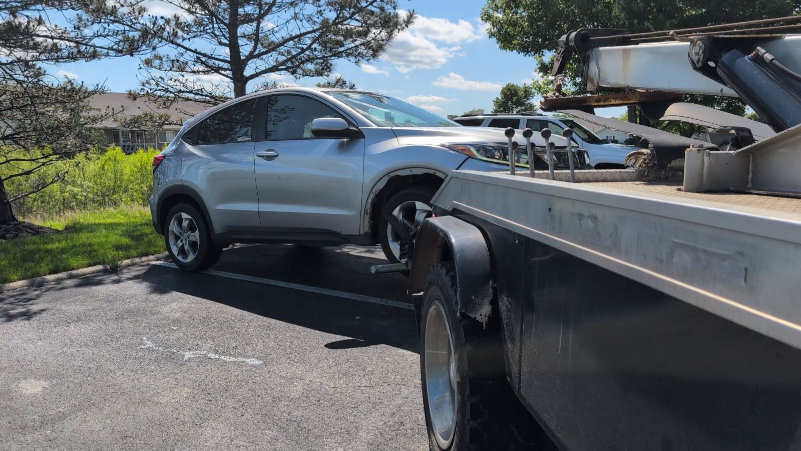 Silver SUV being towed on a flatbed truck beside a road on a sunny day