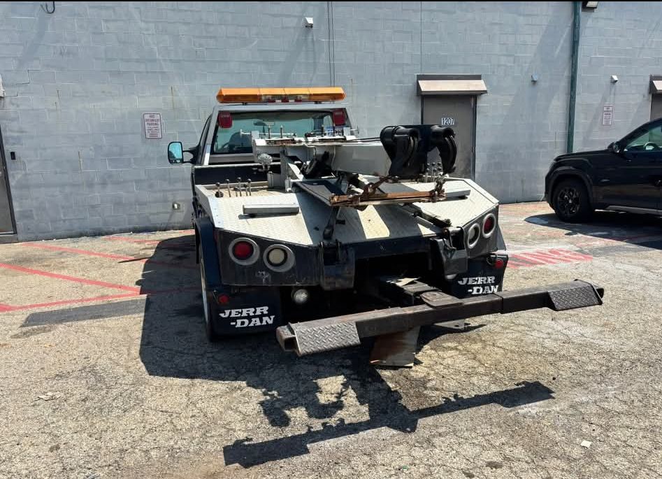 Tow truck with damaged front end parked against a gray wall in a lot