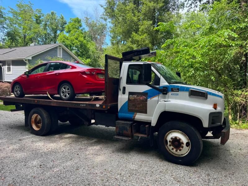 Tow truck hauling a red sports car on a flatbed in a wooded driveway