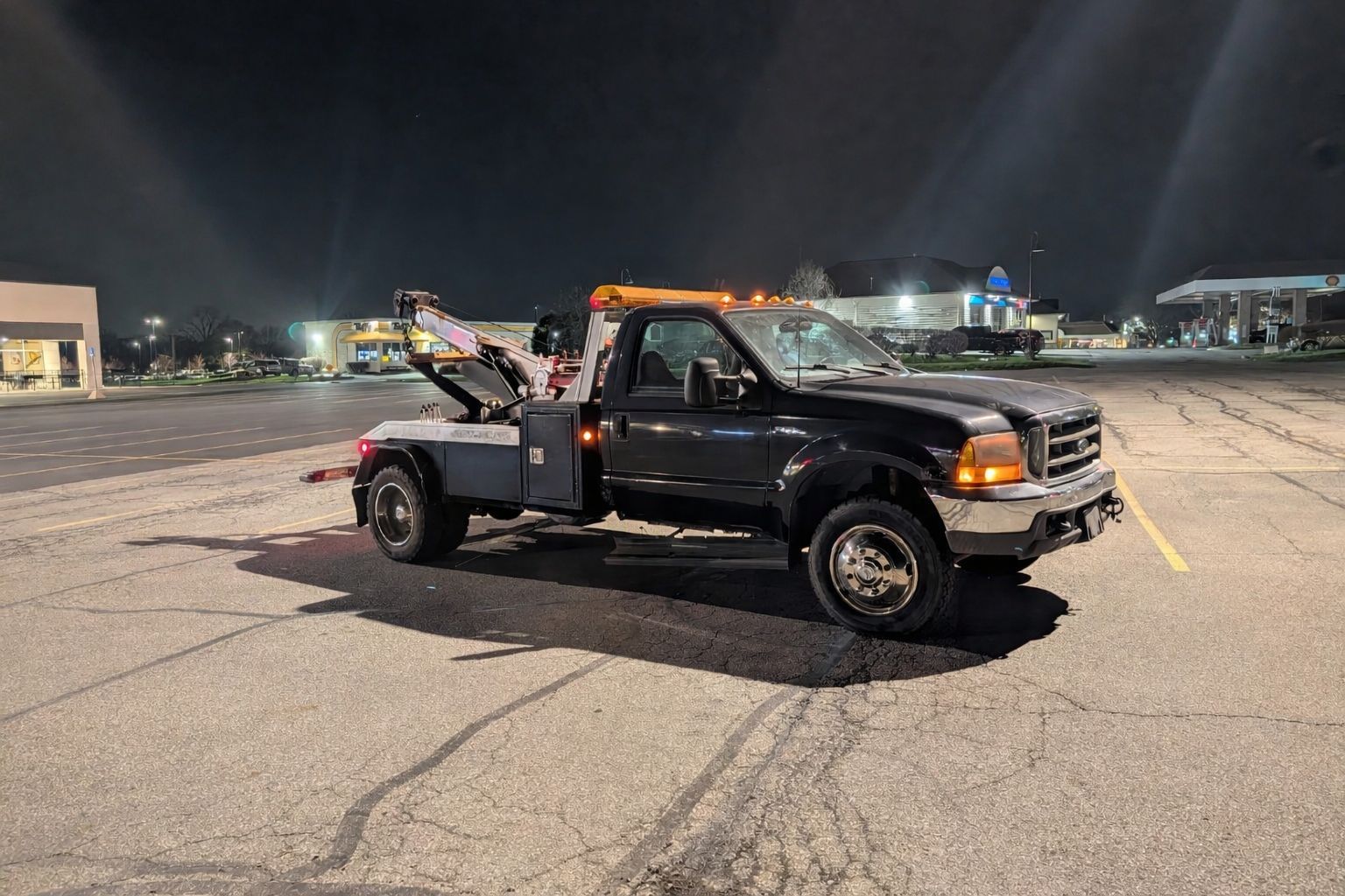 Black tow truck parked in a lit parking lot at night