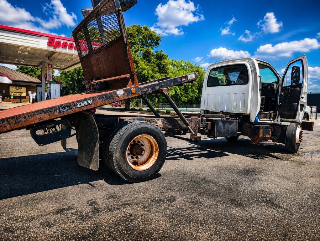 White dump truck with tilted flatbed parked at a gas station under a blue sky