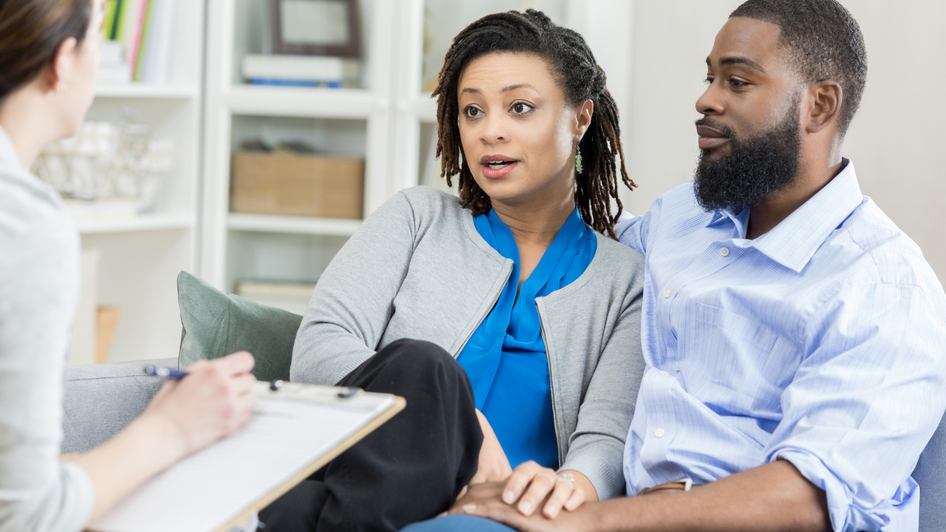 Two people seated in a counseling session, listening to an off-screen therapist in a bright office.