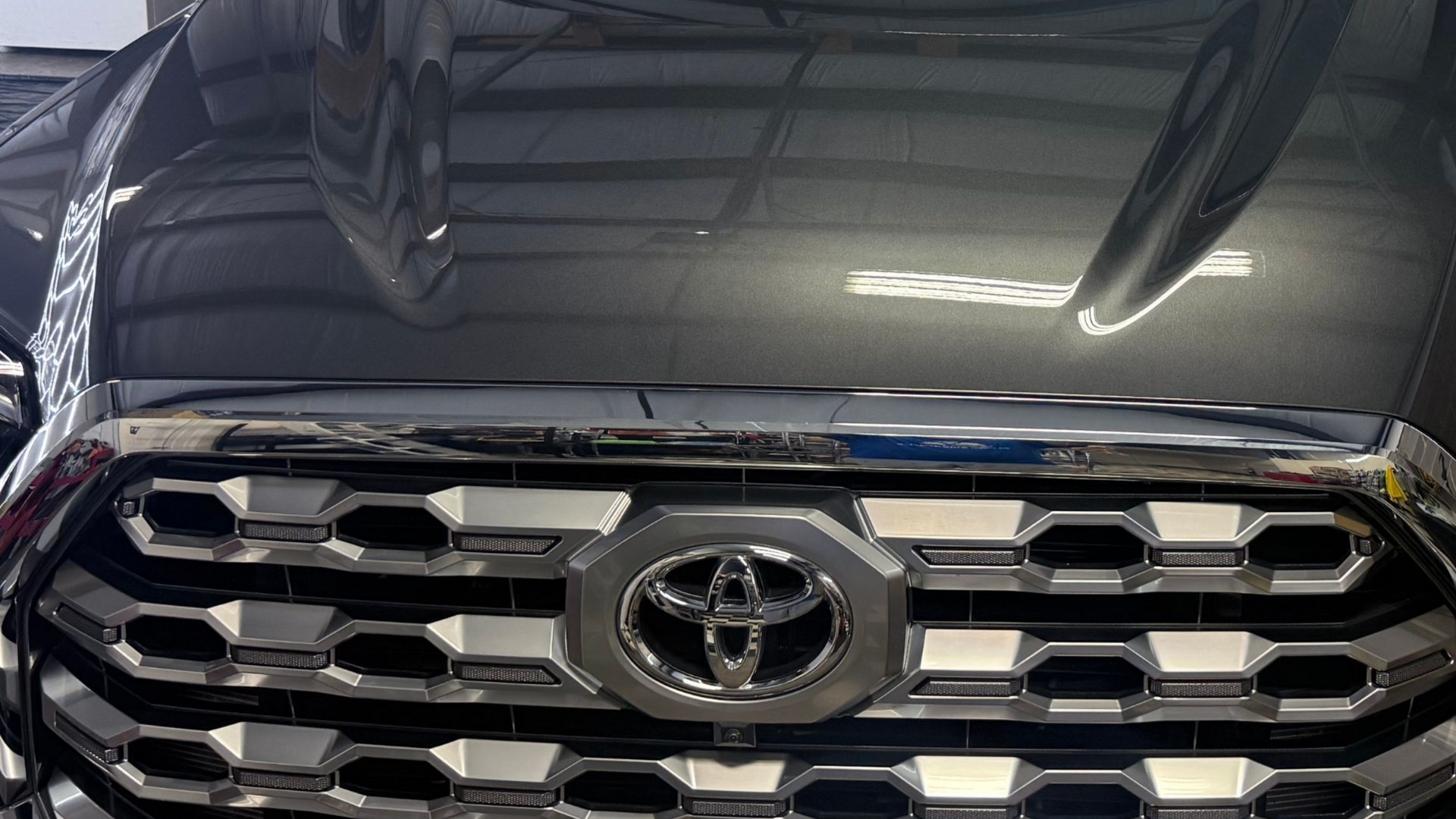 Close-up of a black Toyota SUV grille and emblem, with the hood open