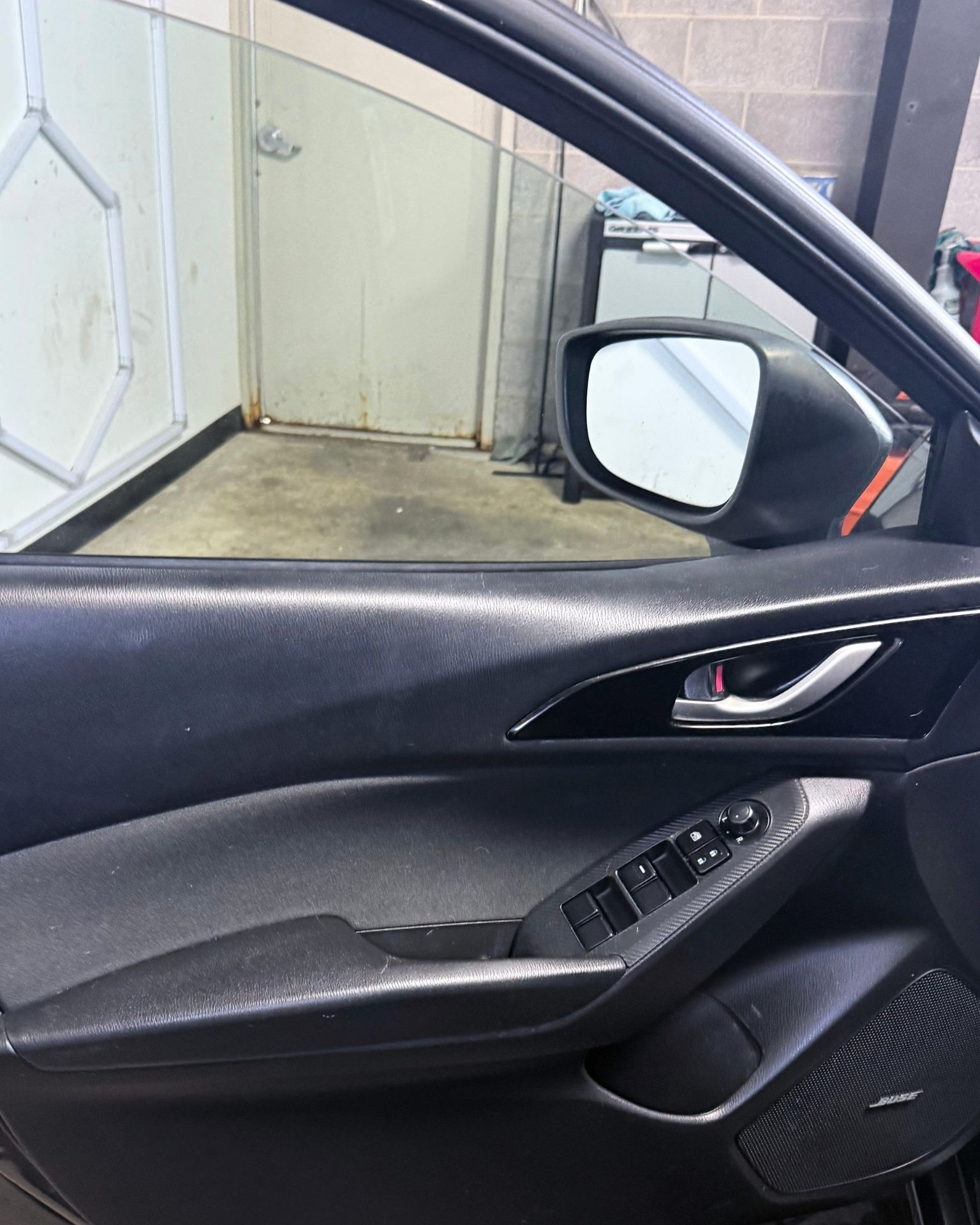 Car door interior with window controls and side mirror, parked beside a wall in a narrow outdoor space