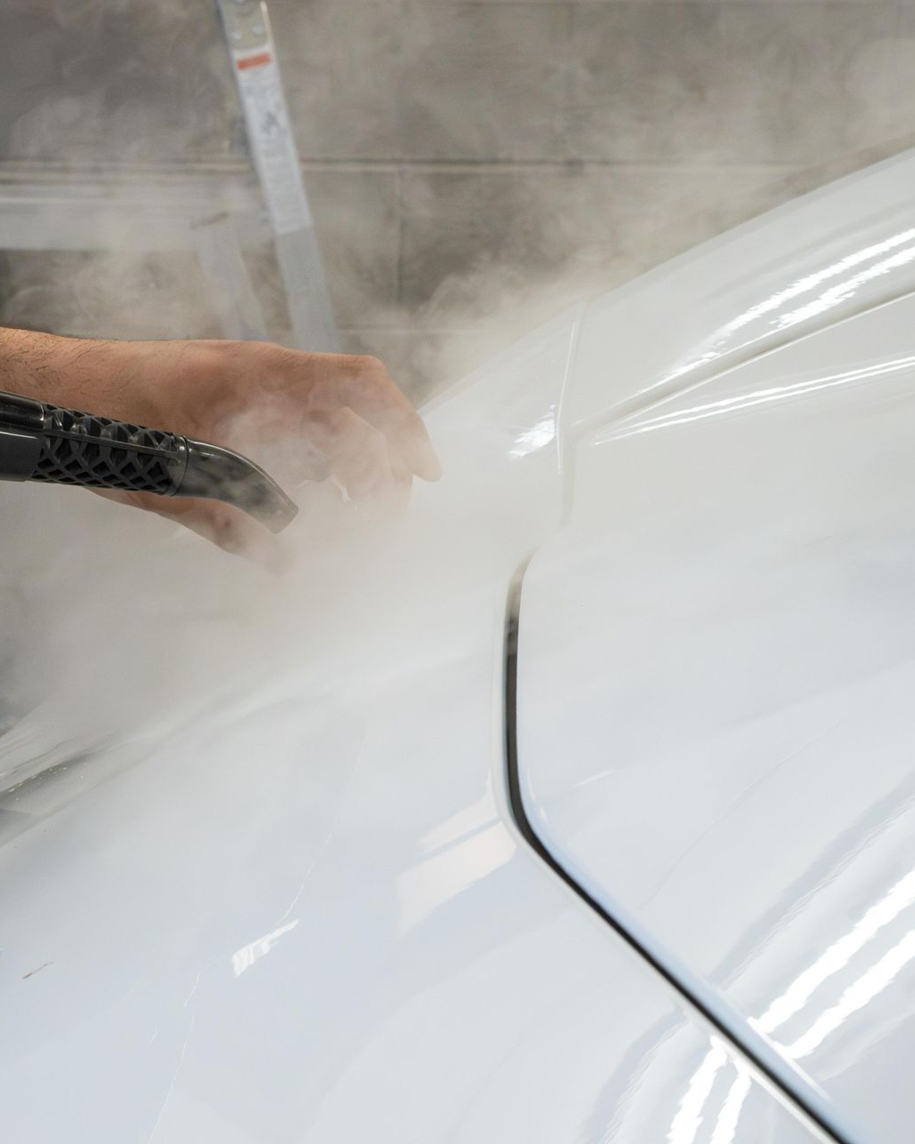 Person pressure-washing a white car, creating a cloud of spray and mist