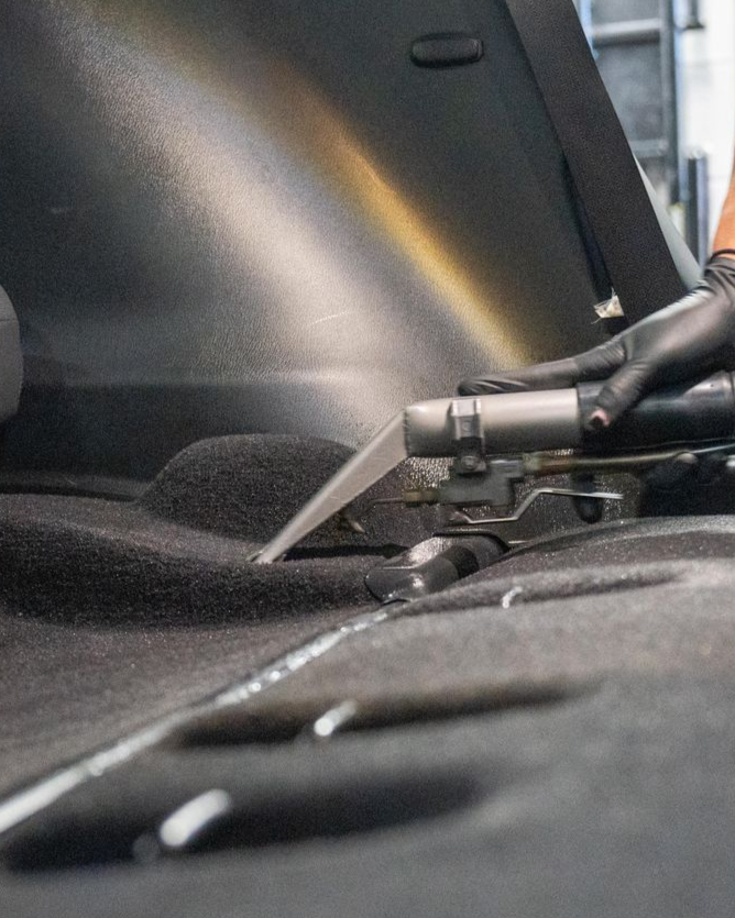 Black-gloved hand using a vacuum nozzle to clean a car interior