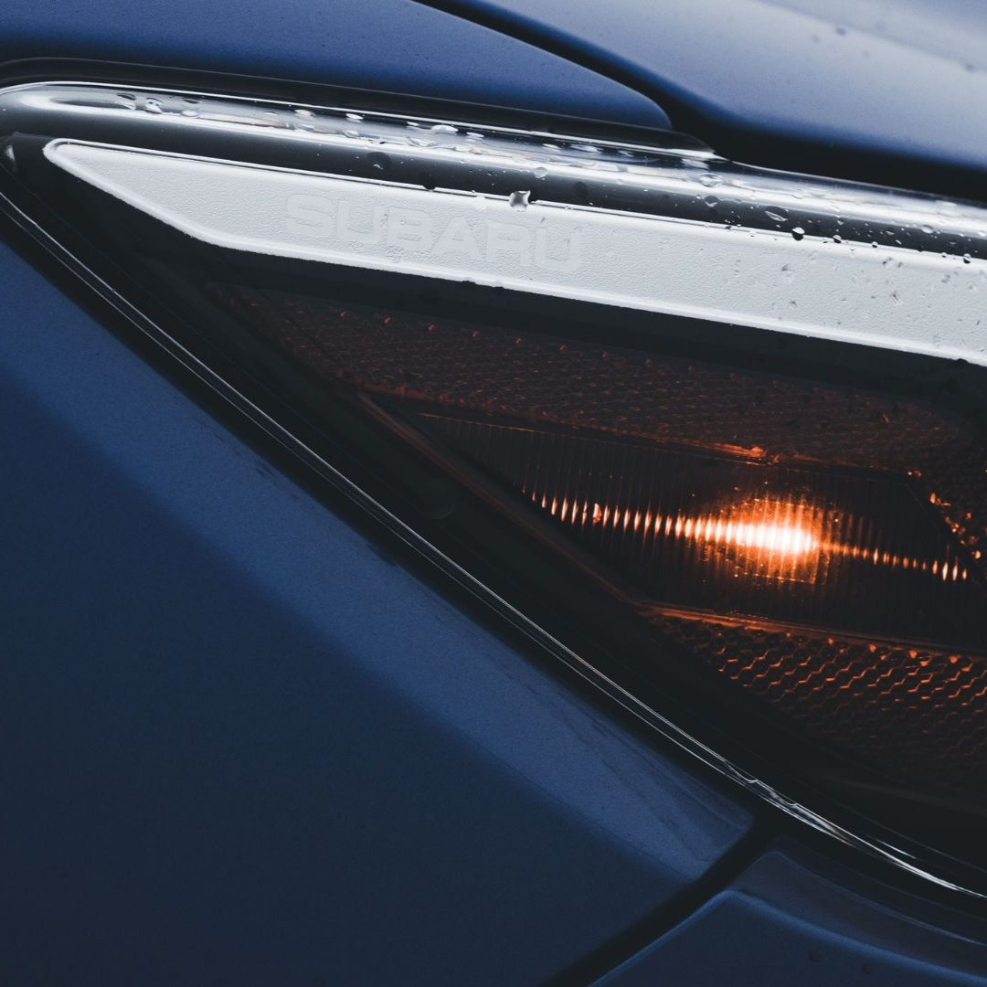 Close-up of a blue car’s front headlight with a bright amber light glowing inside