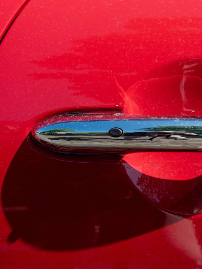 Close-up of a chrome car door handle on a red vehicle, with reflections visible on the handle.