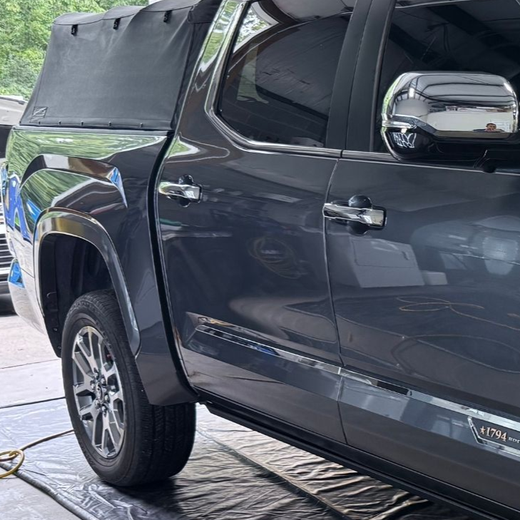 Dark gray pickup truck with camper shell parked indoors, side view.