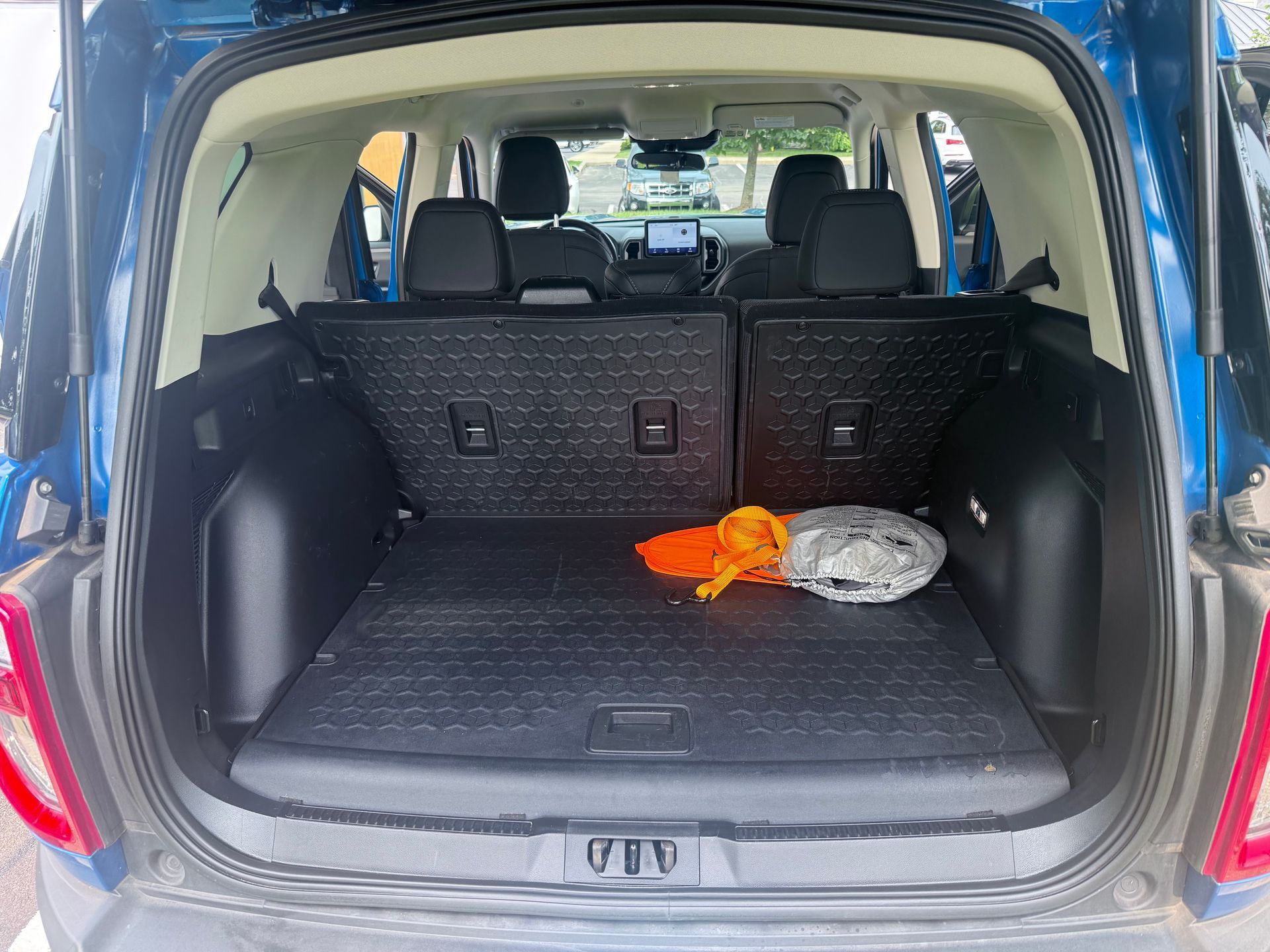 Open SUV trunk with folded rear seats, black cargo mat, orange cloth, and a gray bag inside.