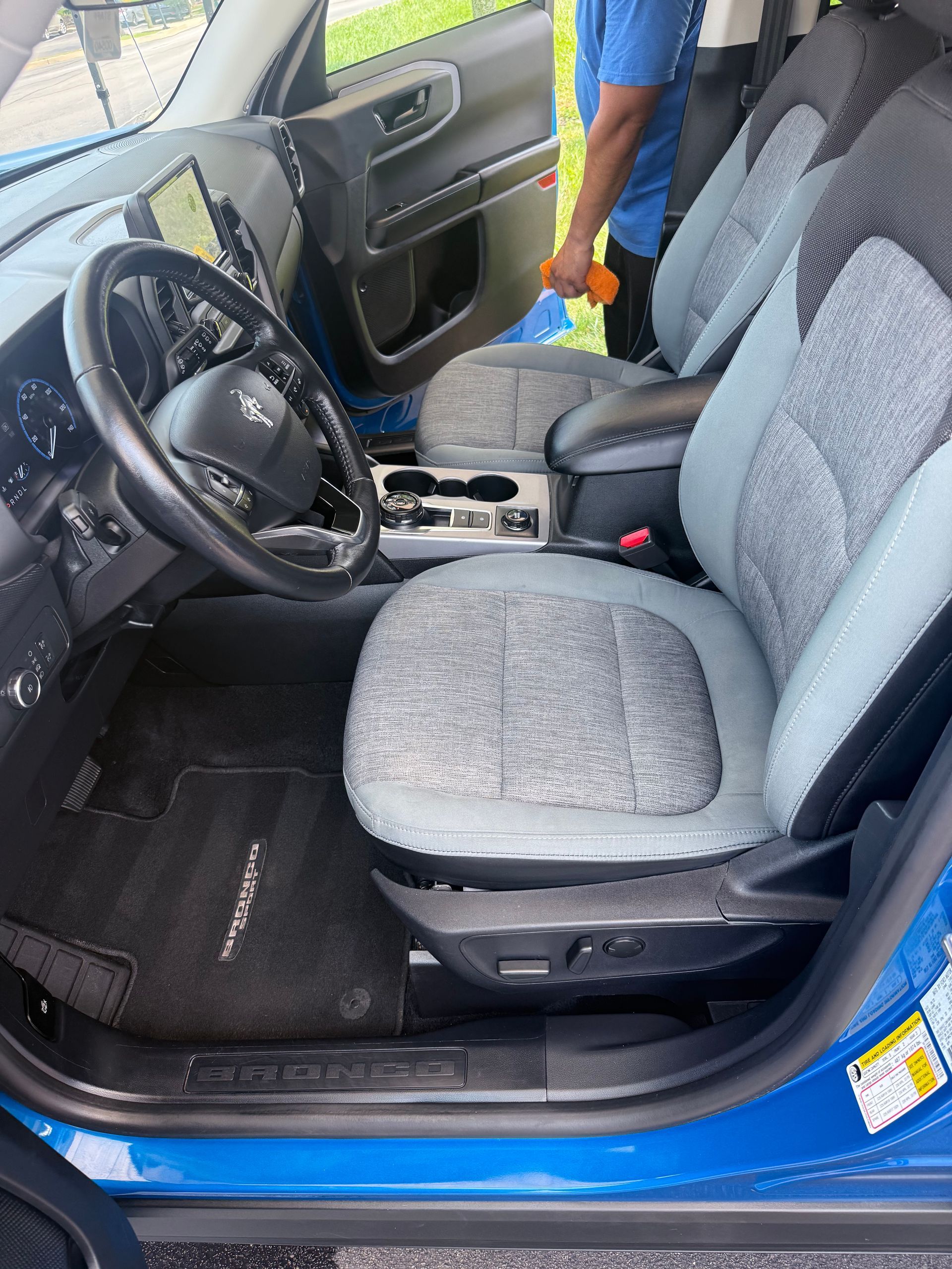 Blue car interior with gray seats and open driver door, showing the steering wheel and center console
