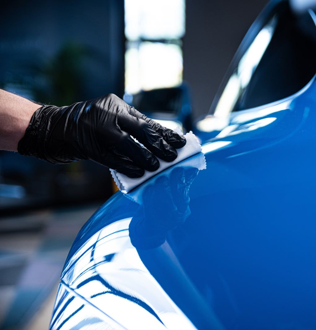 Gloved hand polishing a glossy blue car body with a cloth