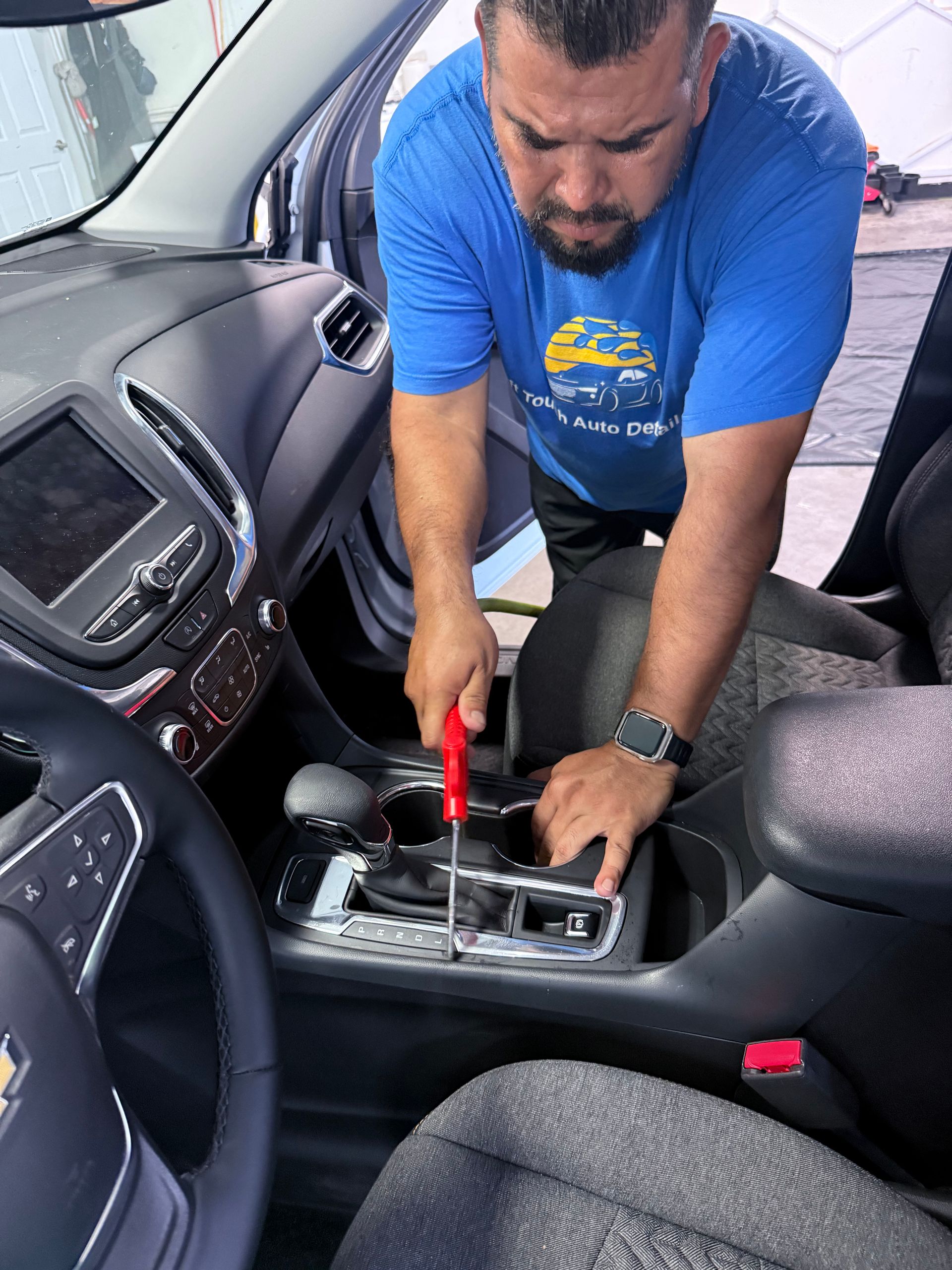 Mechanic using a red screwdriver to work on a car’s center console inside the front seat area