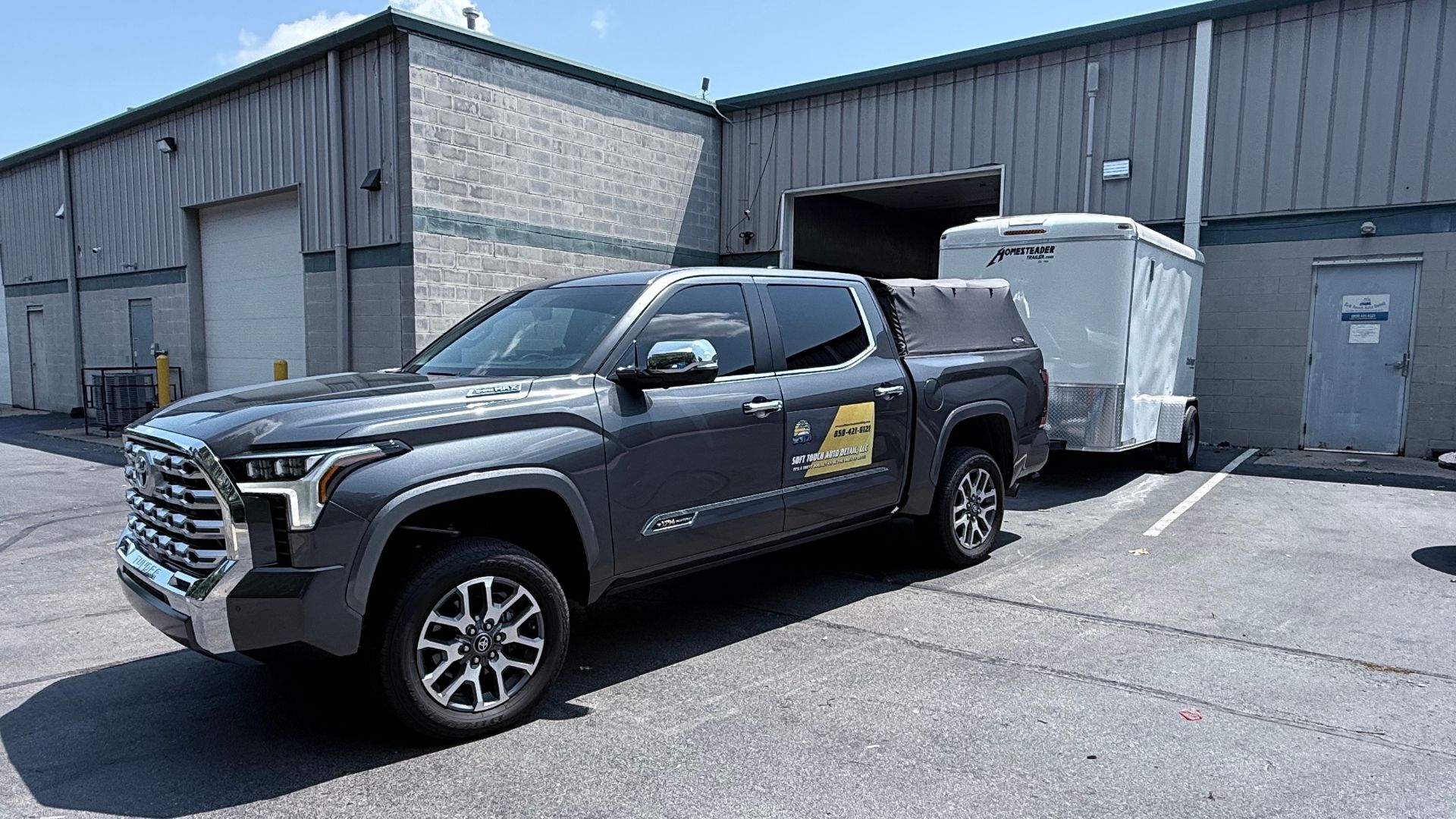 Black pickup truck parked beside a gray industrial building and white trailer in a lot.