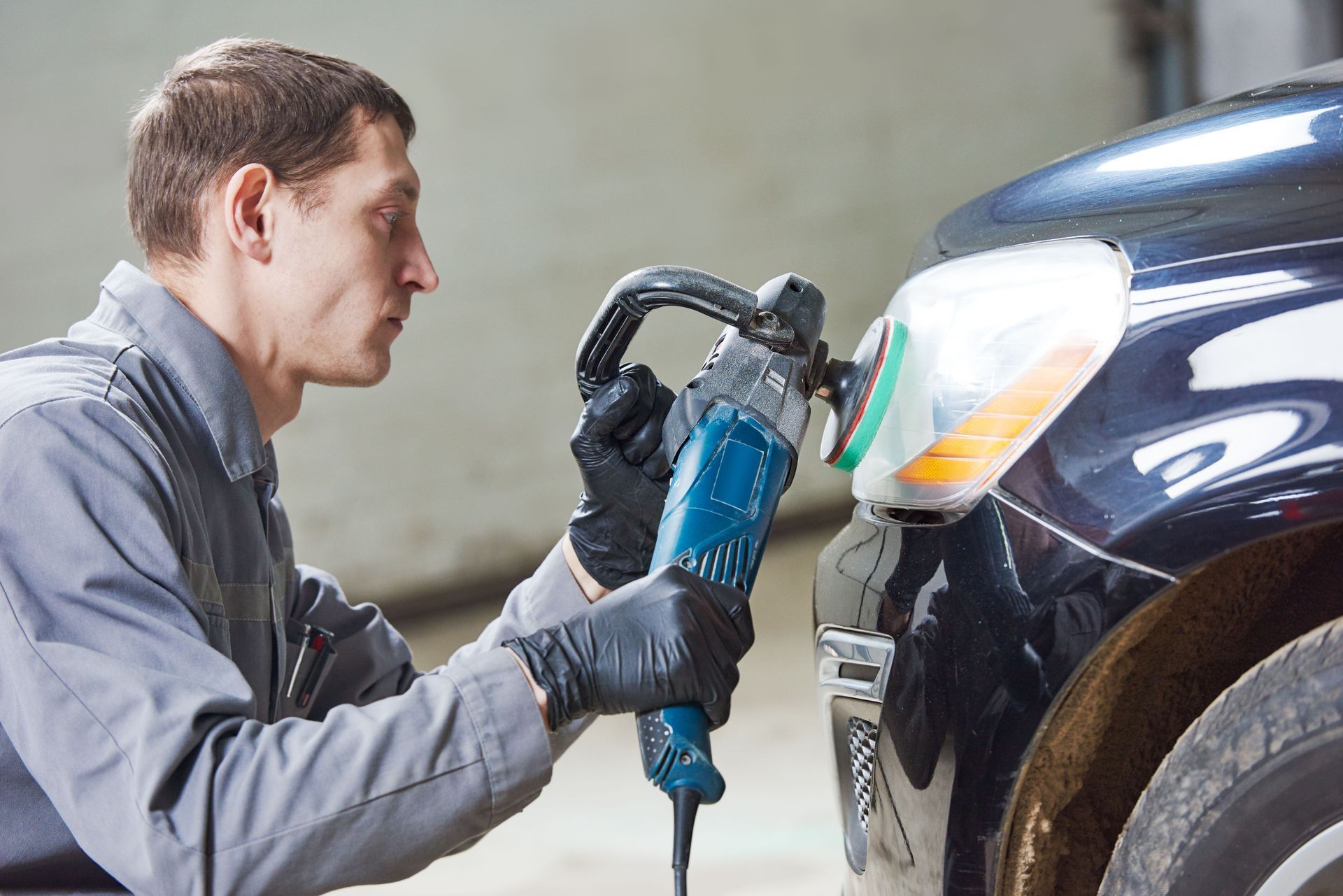 Mechanic polishing a car’s front bumper with a buffer in a garage