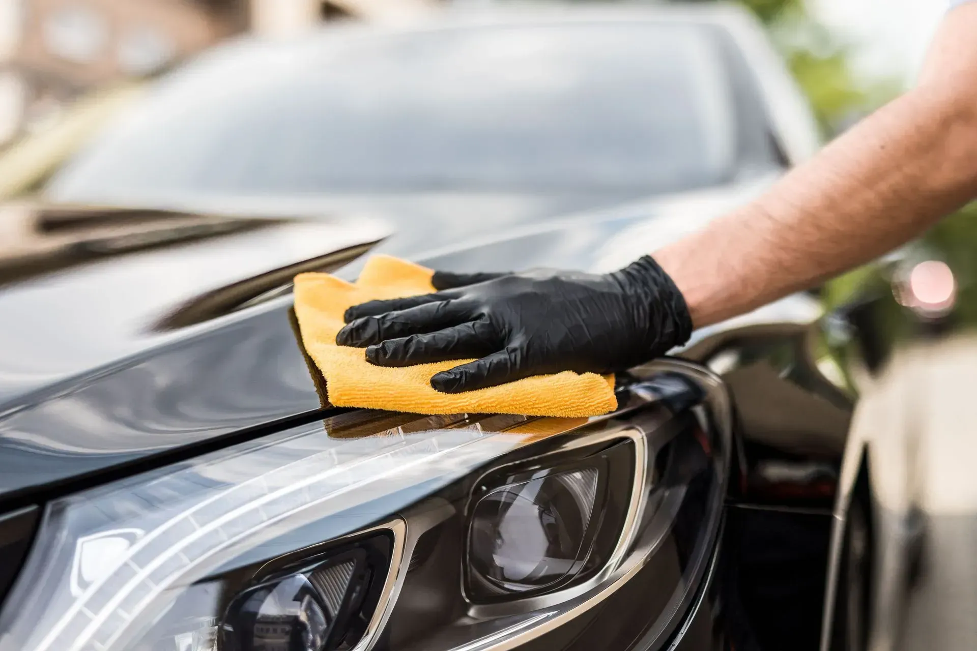 Gloved hand wiping a black car’s hood with a yellow cloth