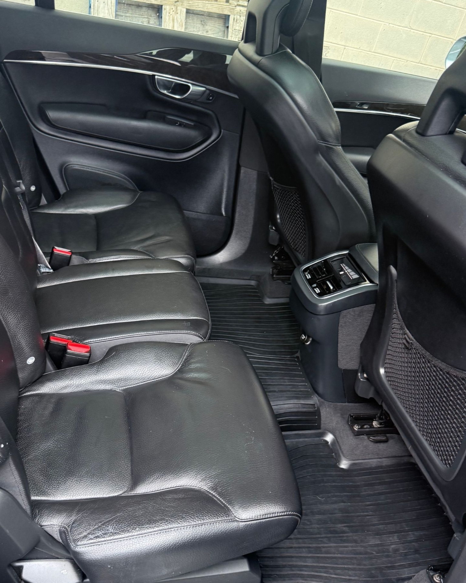 Car interior rear seats with black leather upholstery and center console controls, viewed from the back seat