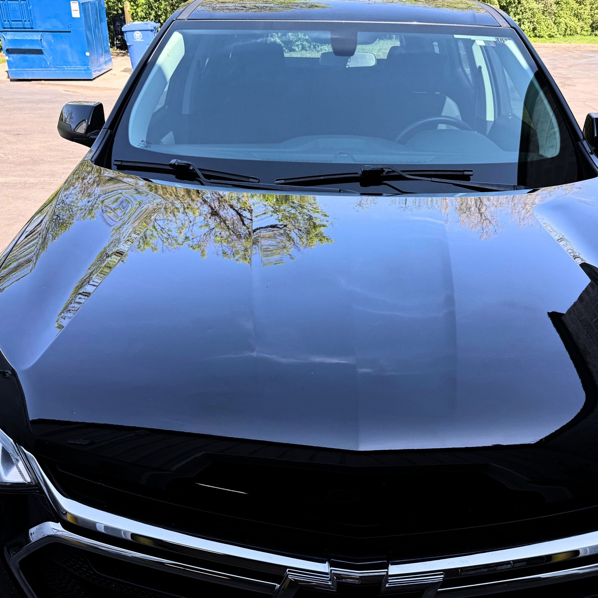 Black sedan parked outdoors, front view with tree reflections on the hood.