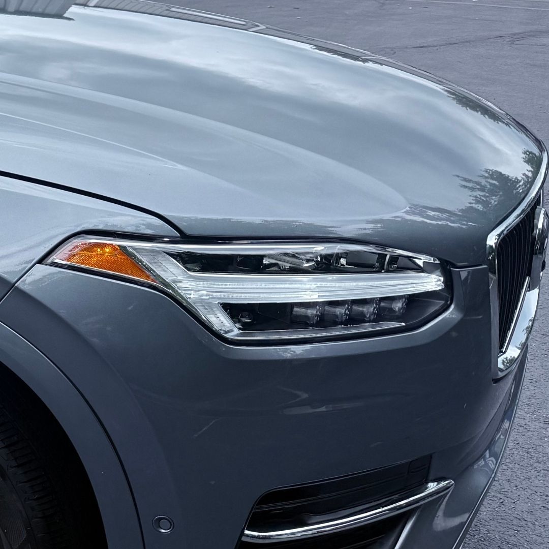 Close-up of a gray car’s front headlight and grille on wet pavement