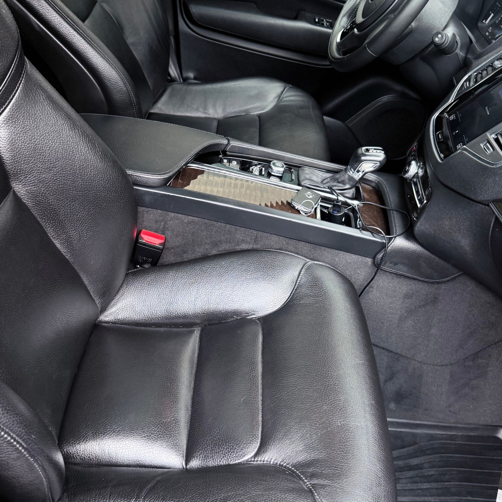 Black leather car interior with a damaged center console and exposed components between the front seats