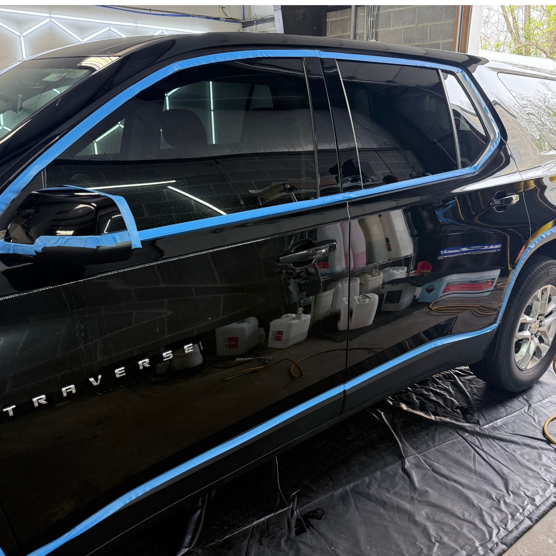 Black SUV in a garage, with blue tape marking the windows and trim for detailing.